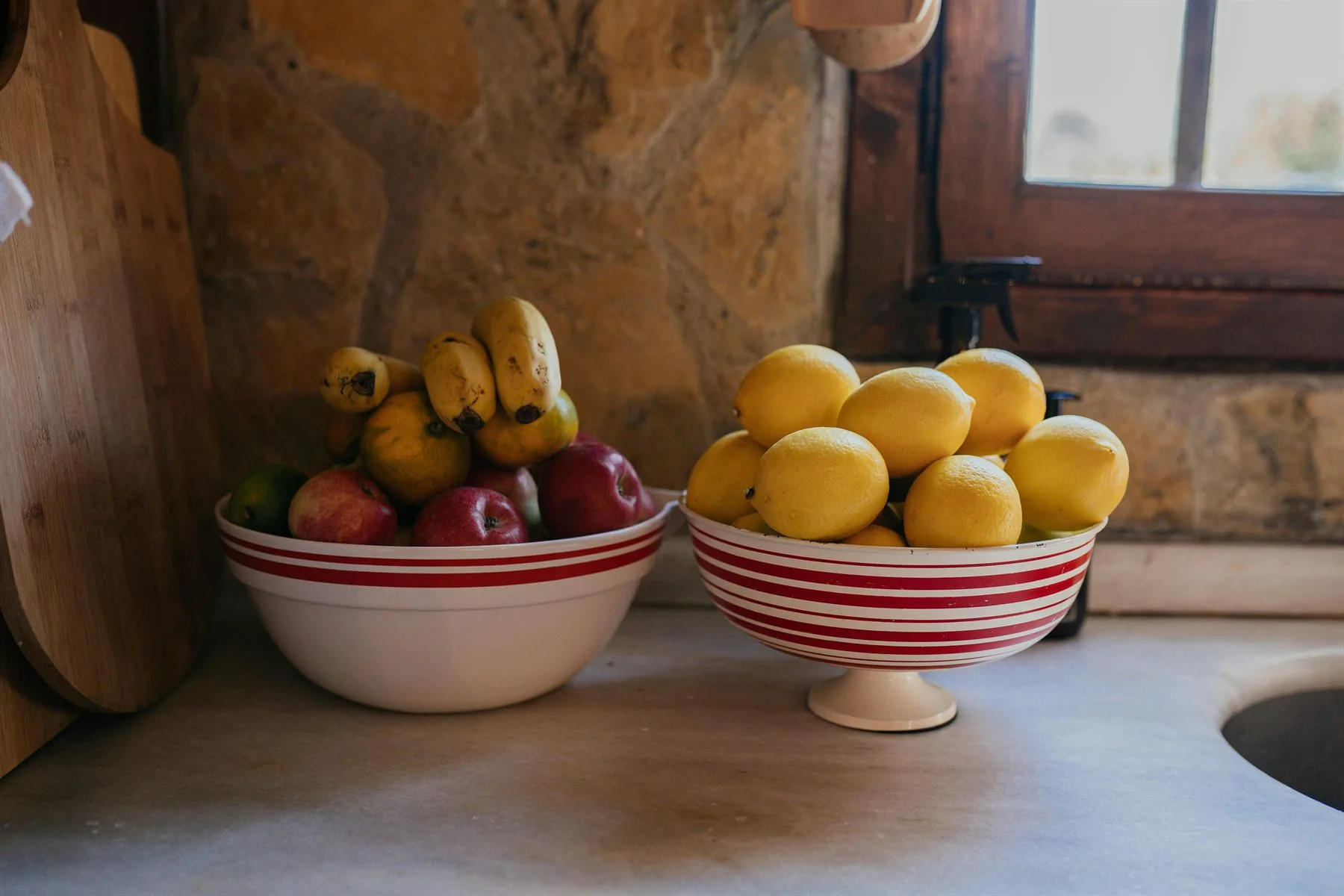 Fruit bowls on a warm table near a window with red, yellow, and golden abundance colors