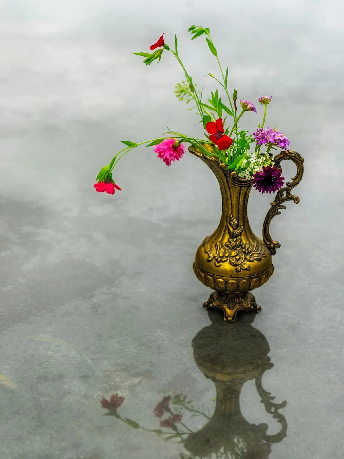 Vintage soft gold vase with colorful flowers against a gray background