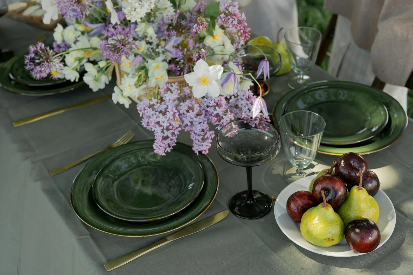 Dining table with dark green plates, gold cutlery, flowers, and fruit