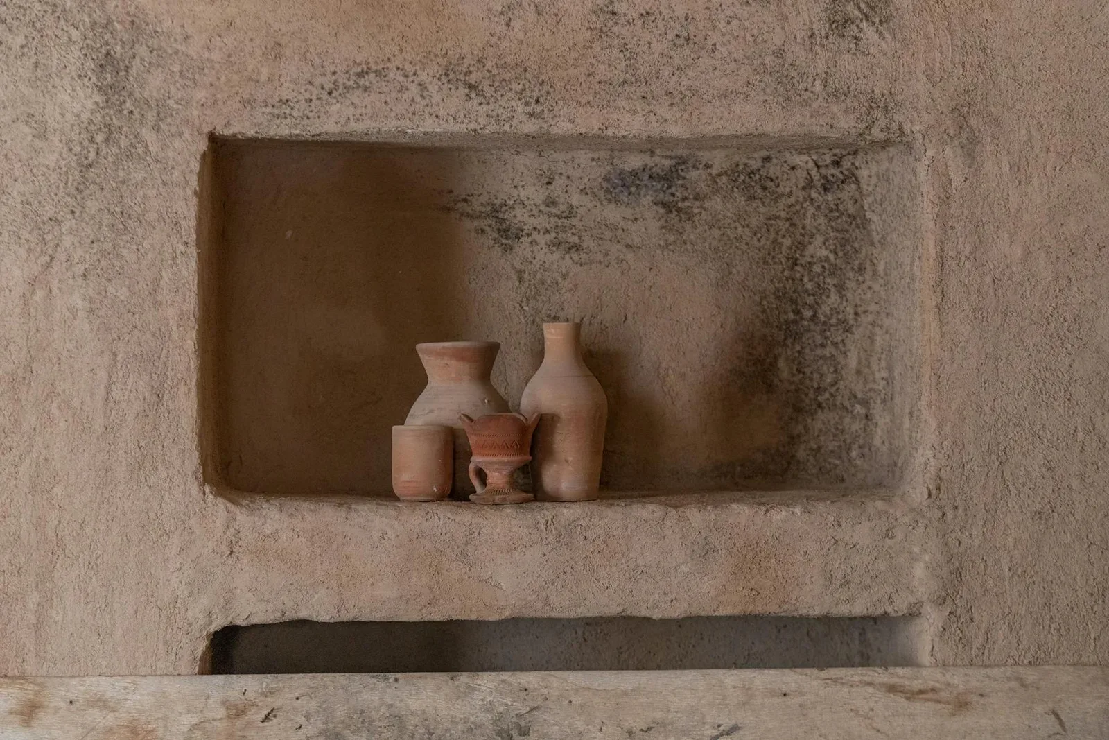 Clay pottery arranged in a textured wall niche with a warm earth tone palette