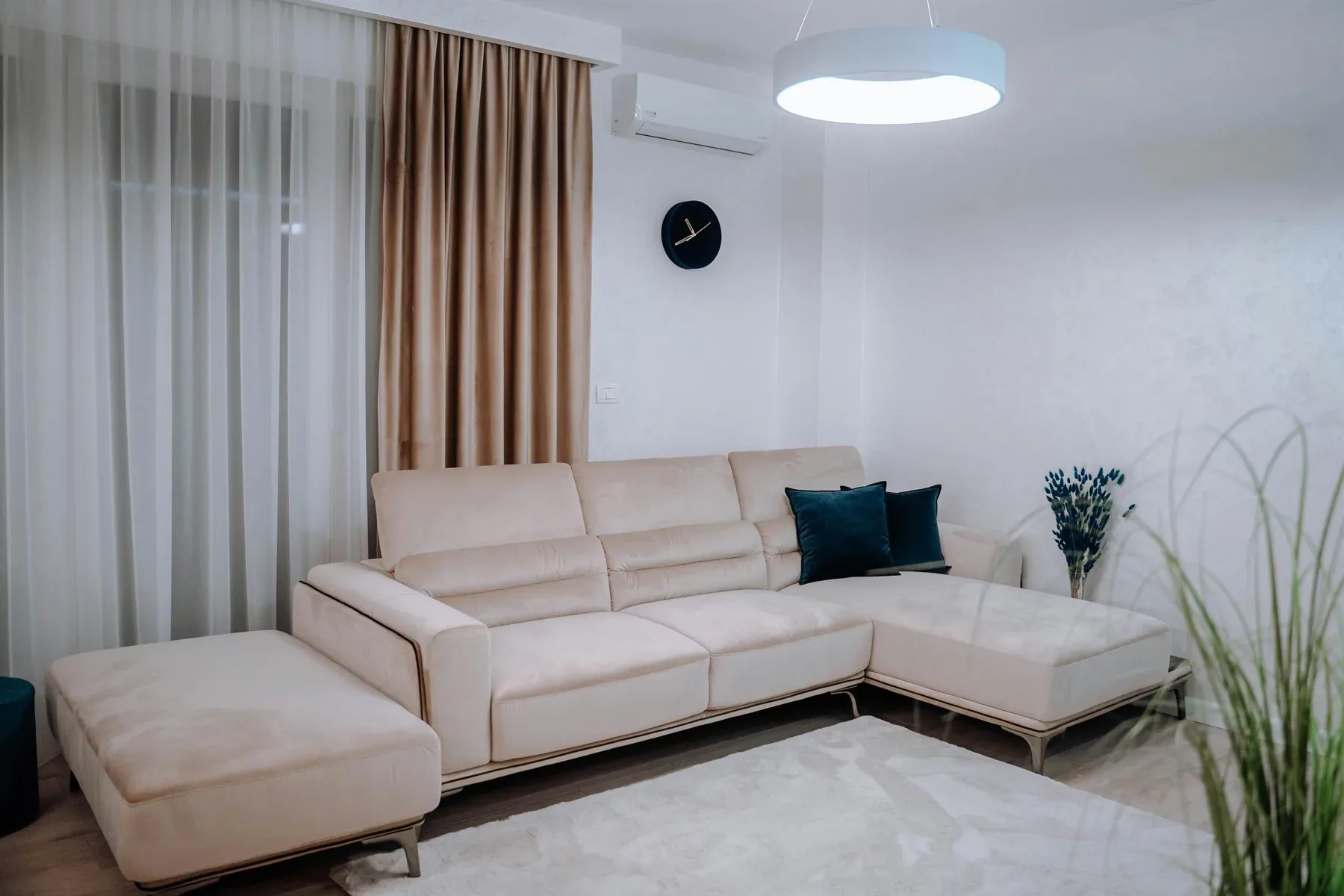 Neutral living room with pale sofa, soft curtains, small plant, and a quiet blue-green accent