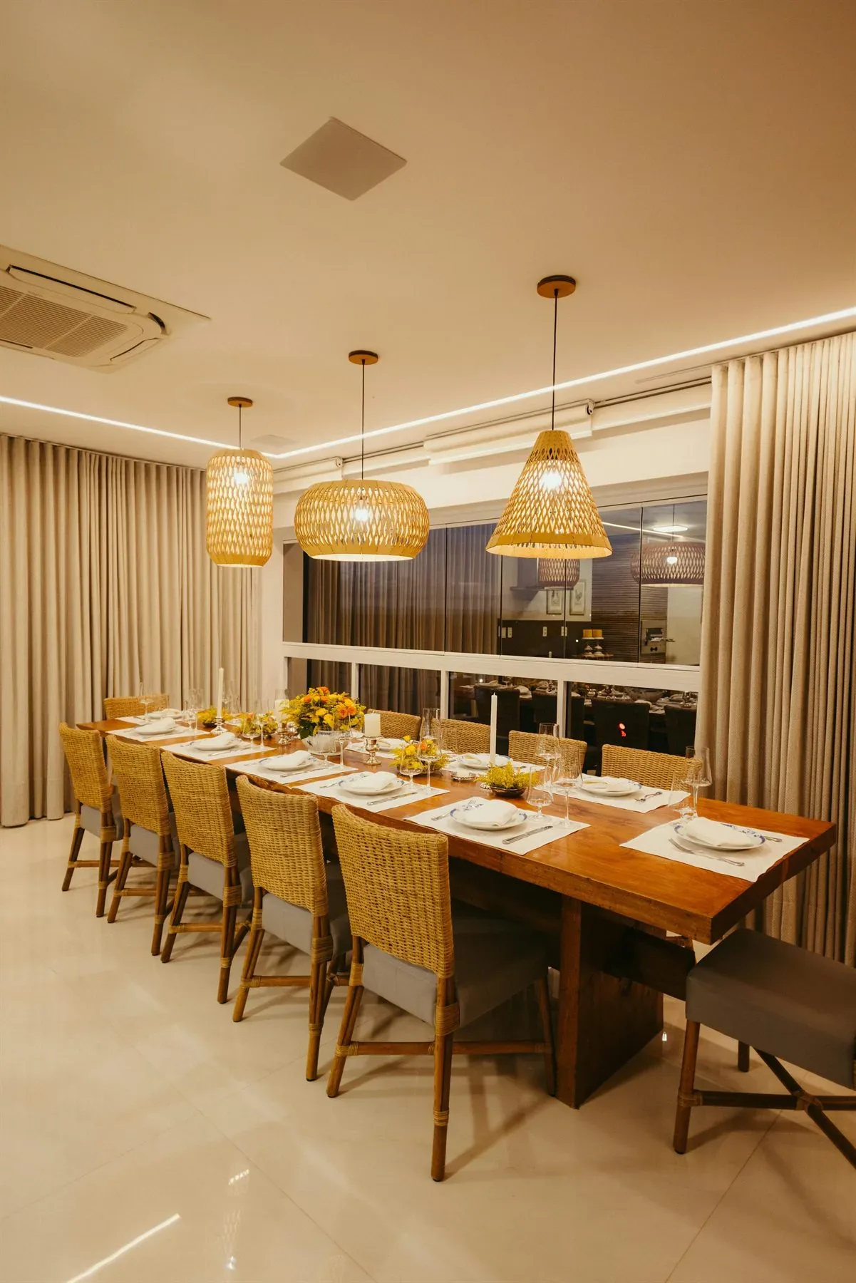 Warm dining room with woven pendant lights, long table, curtains, and layered neutral seating
