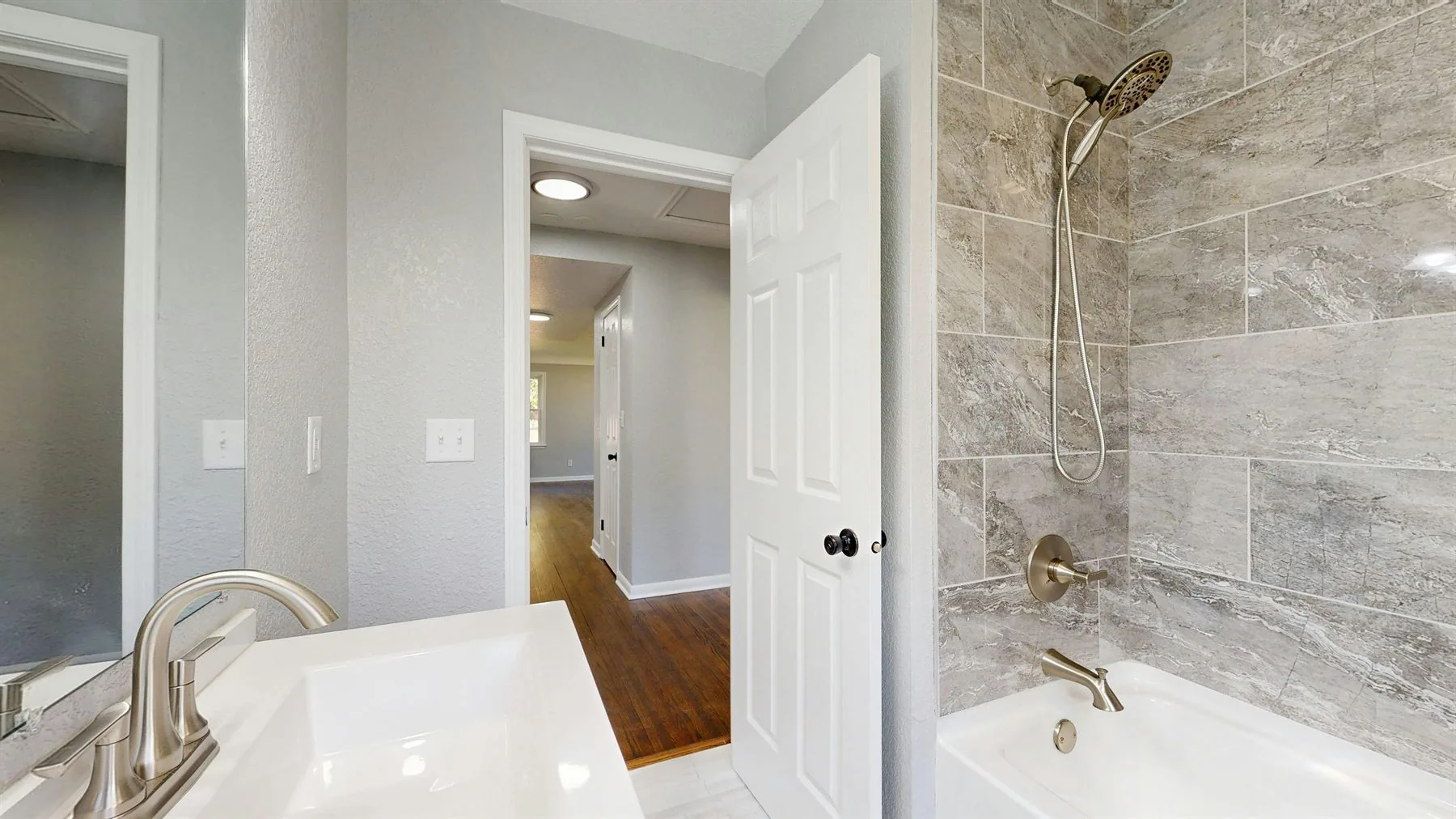 Light gray bathroom with a tiled shower wall, white vanity, and a soft neutral palette