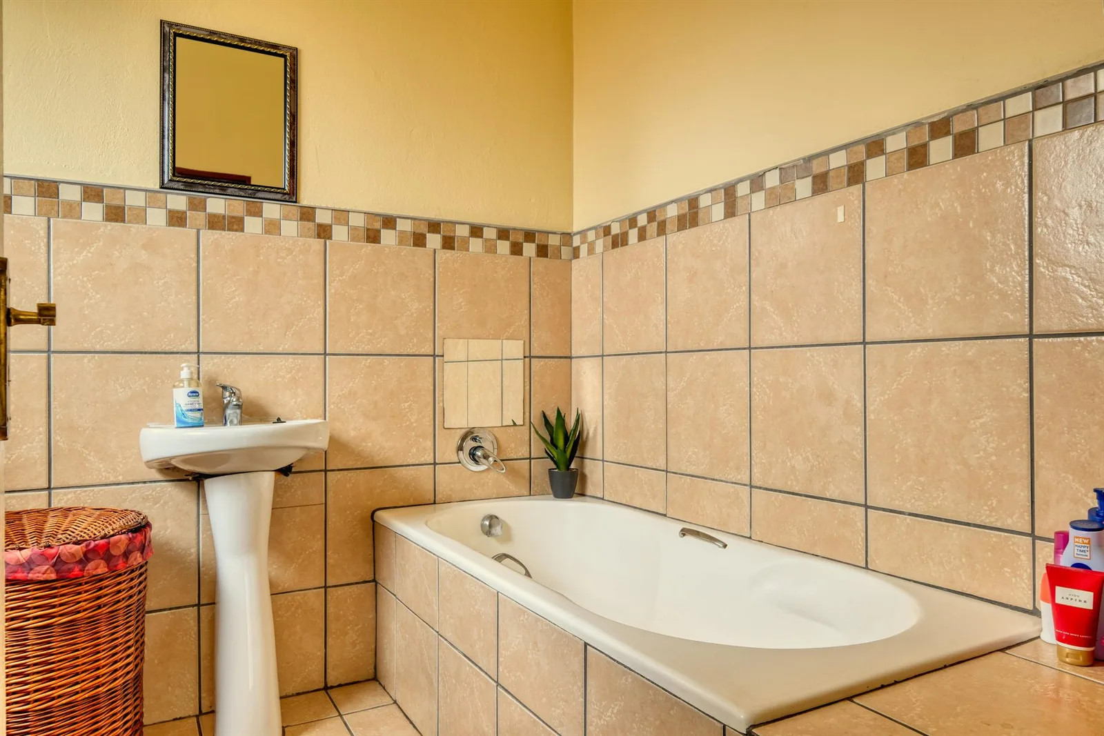 Bathroom with warm beige wall tile, tub, plant, and earthy material palette