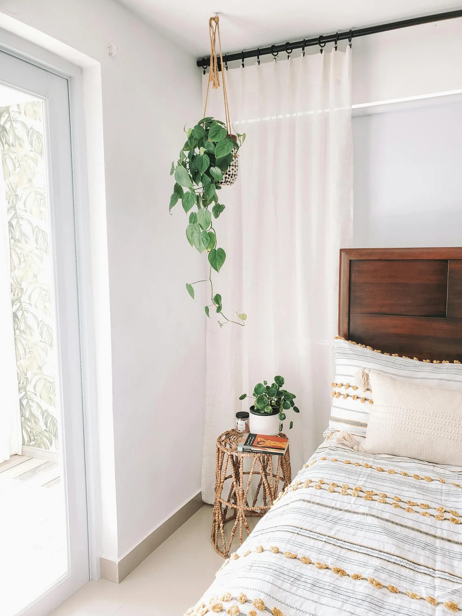 Bedroom with one hanging plant near a window and simple neutral bedding