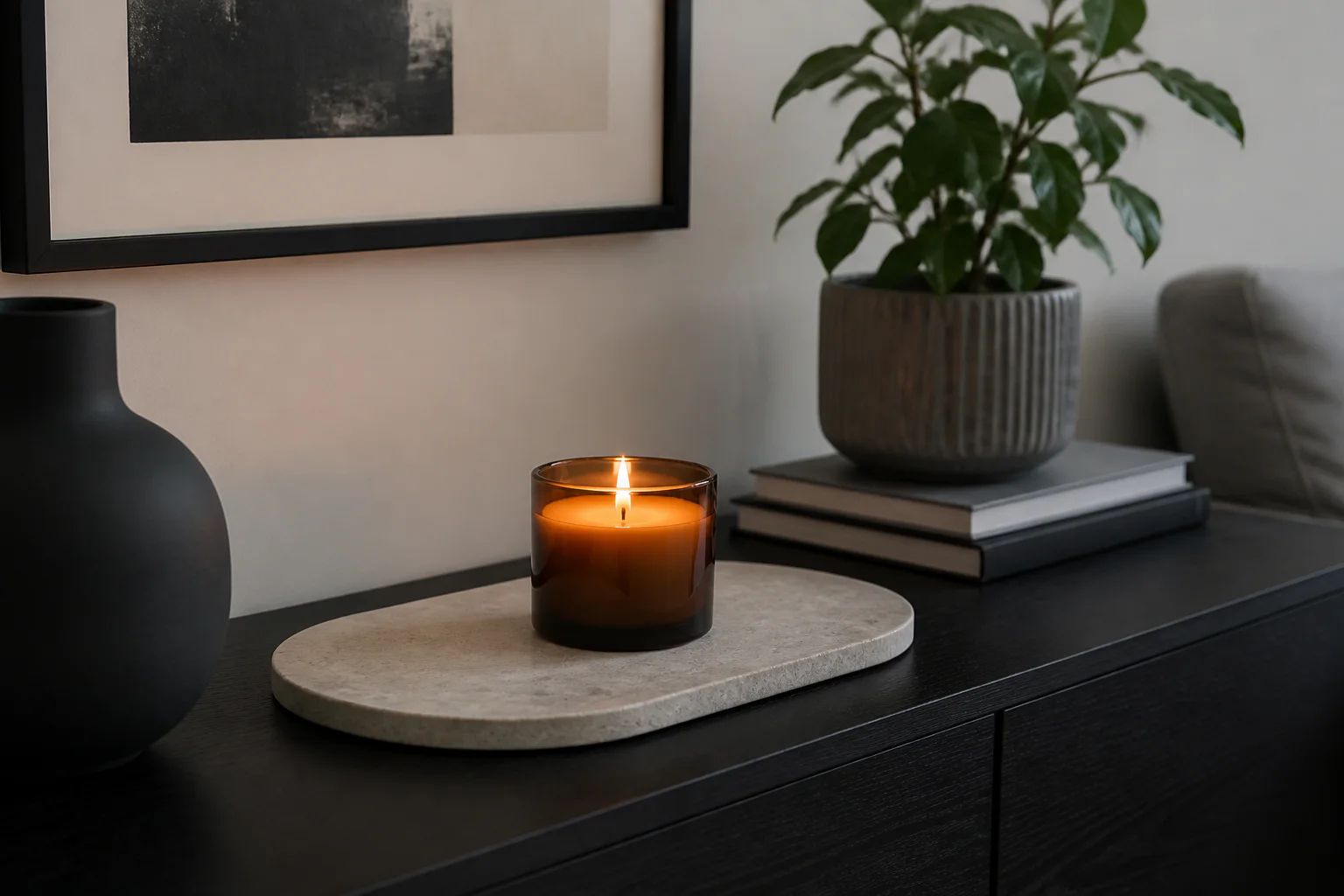 Single amber glass candle on a broad pale stone tray on a black living-room console