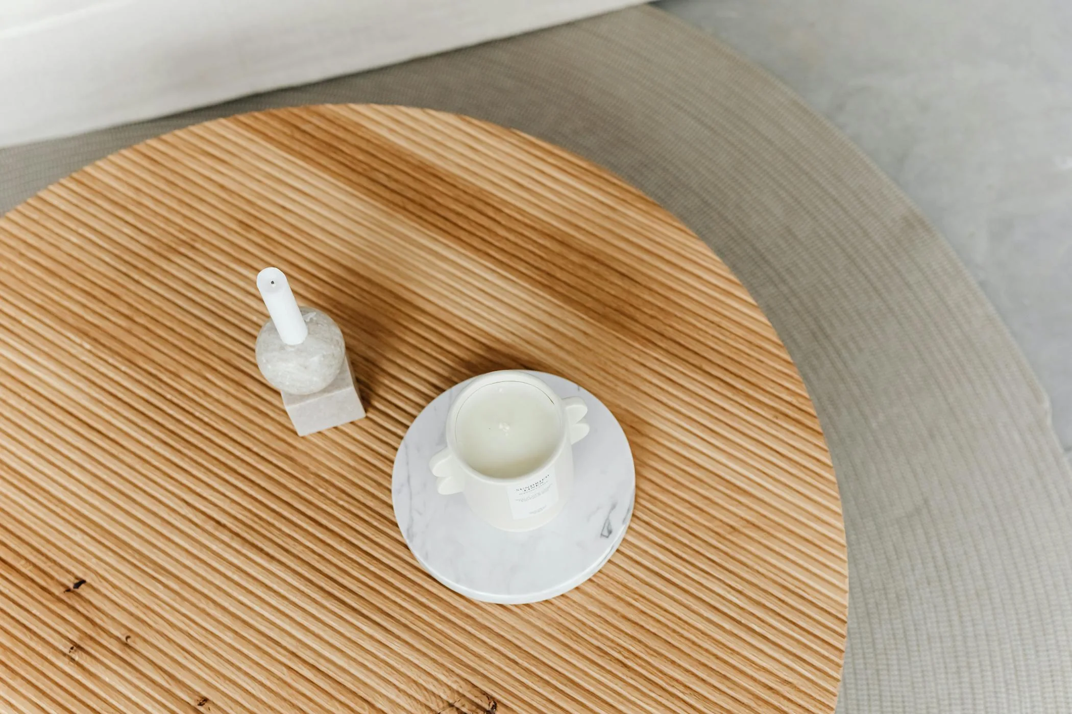 Single candle on a marble tray placed on a pale round wood table