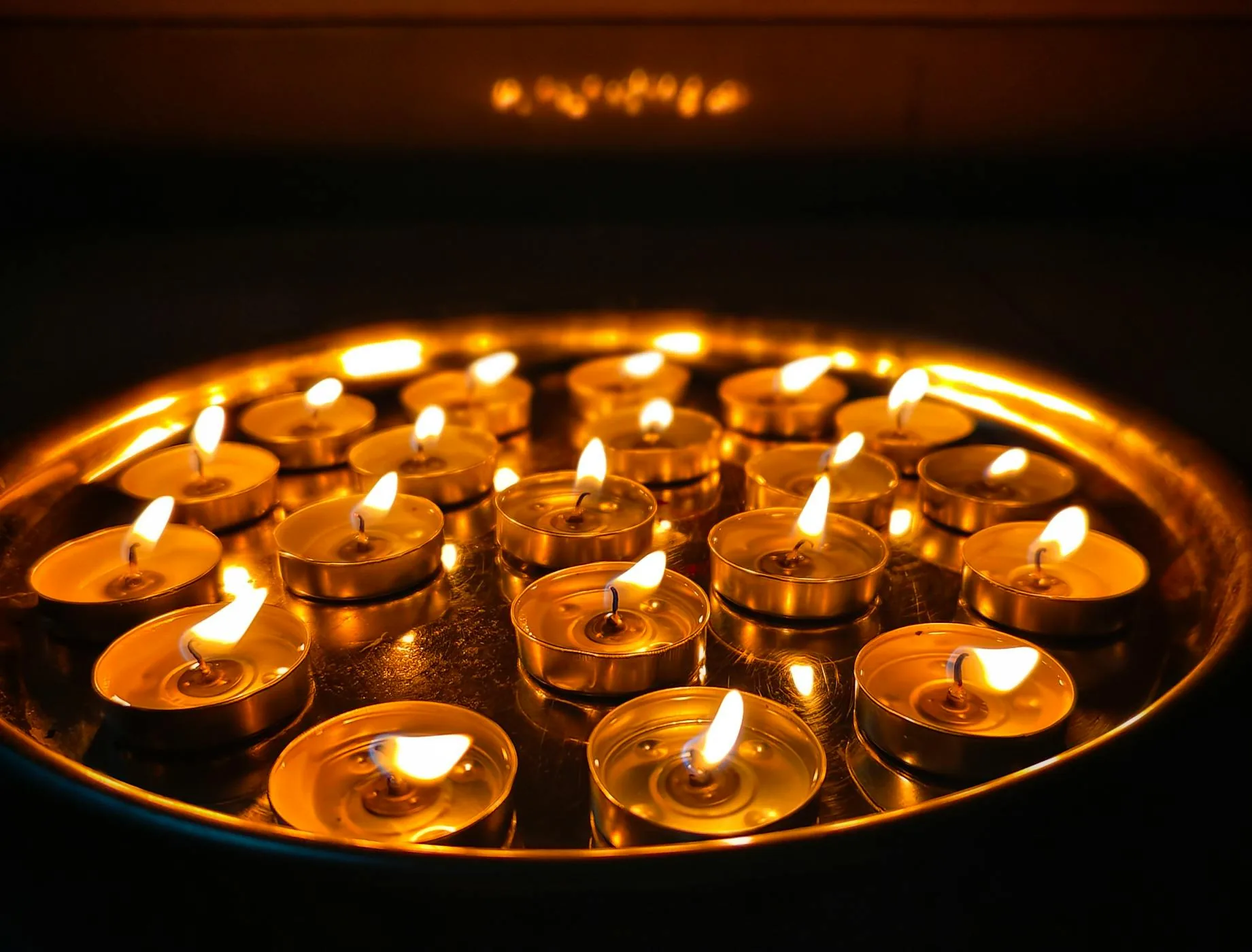 Large group of lit tea lights clustered on a reflective tray in a dark setting