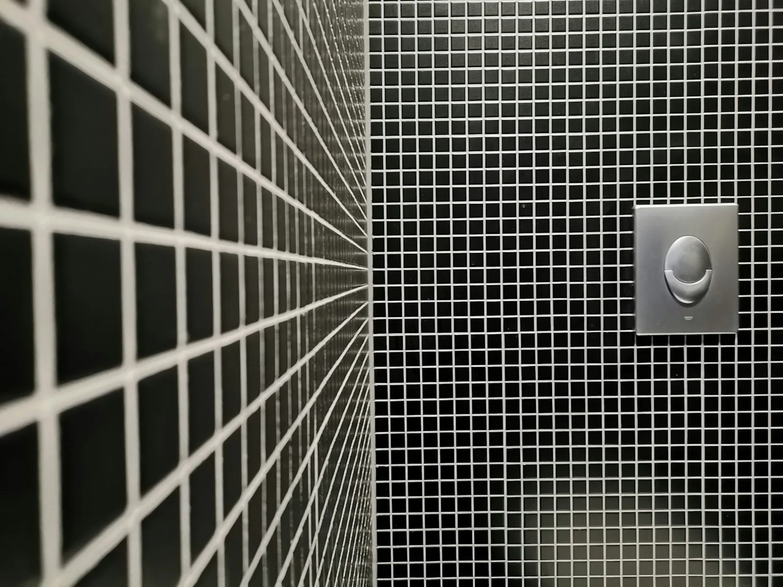 Close view of dark gray bathroom tile and a chrome wall fixture