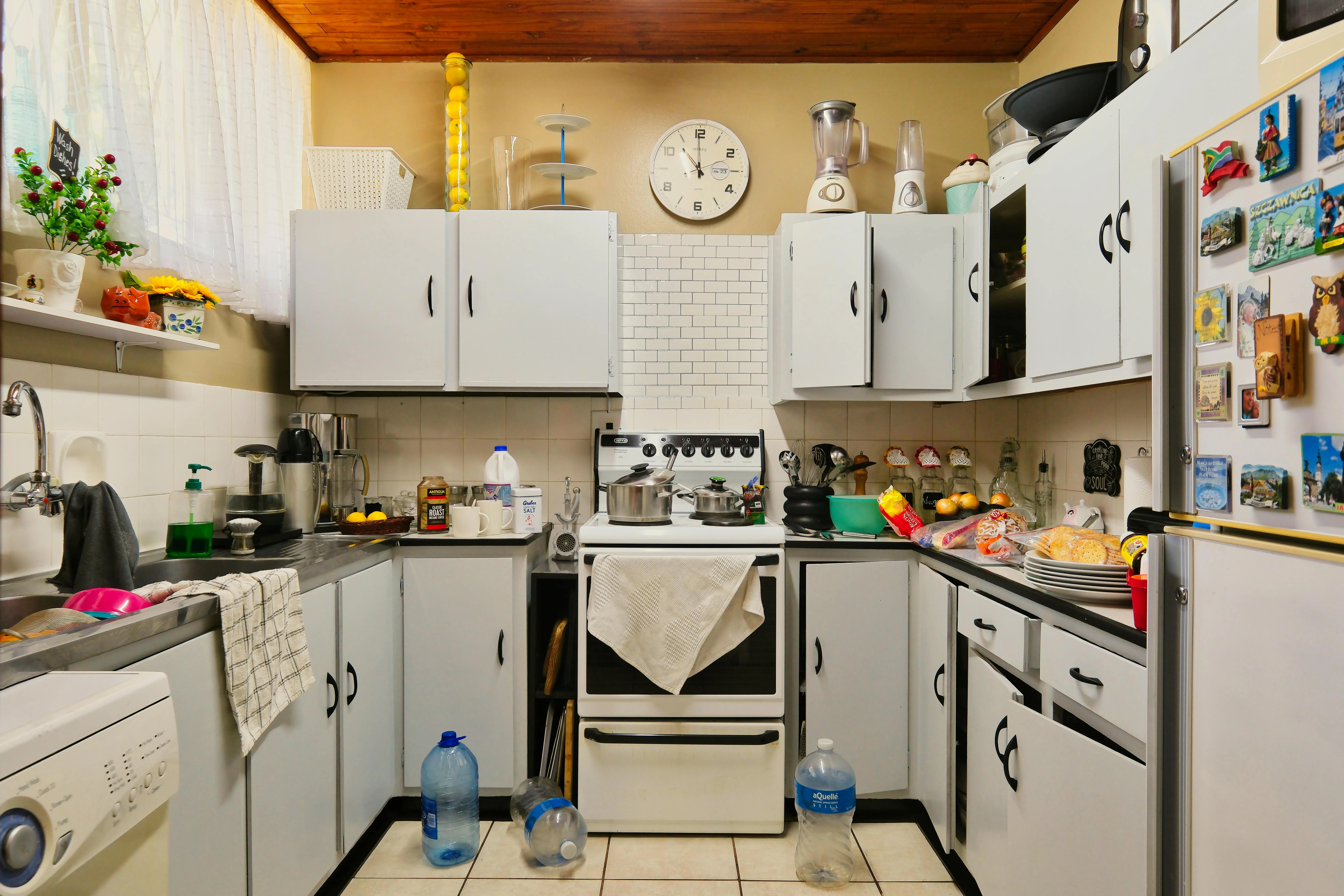 Busy kitchen with cluttered counters, crowded appliances, and everyday overflow on major surfaces