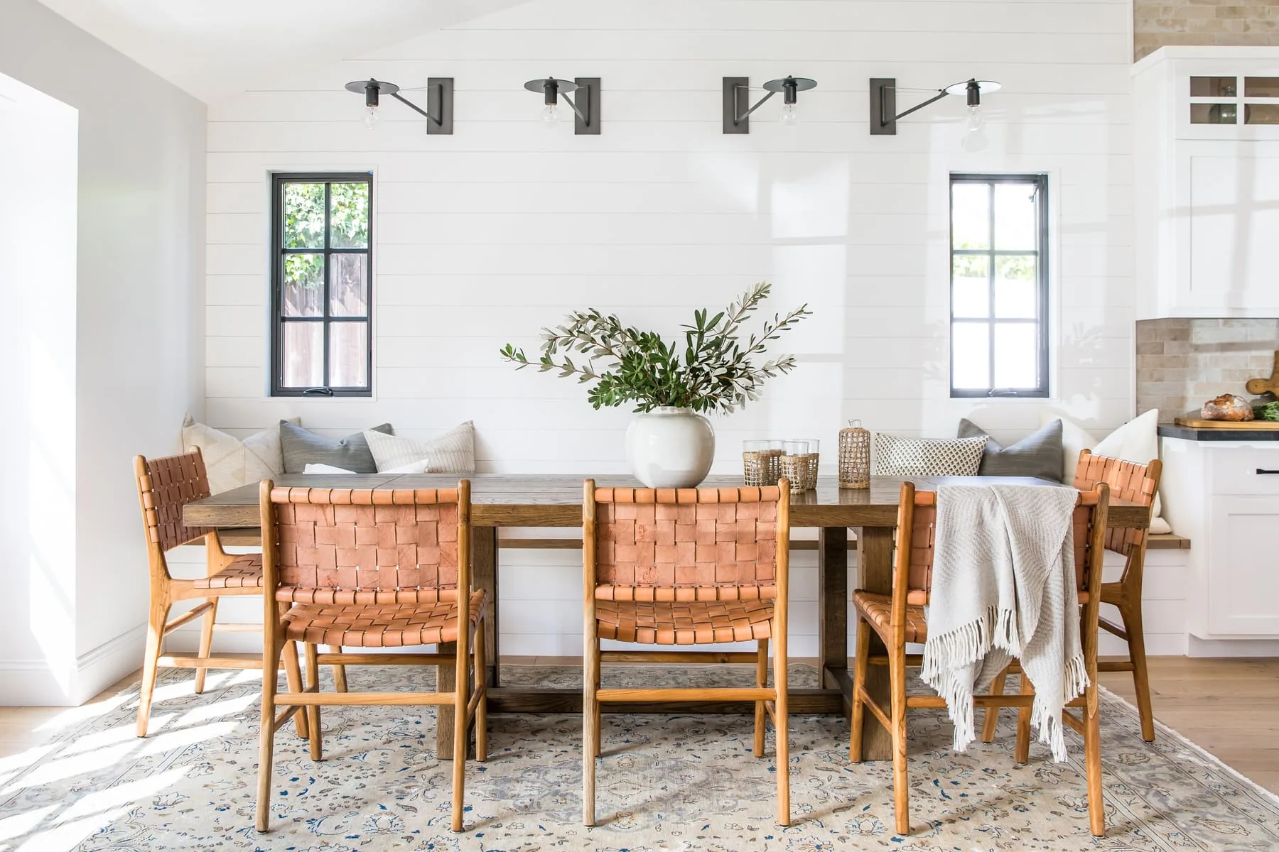 Long wood dining table with woven chairs and soft wall sconces