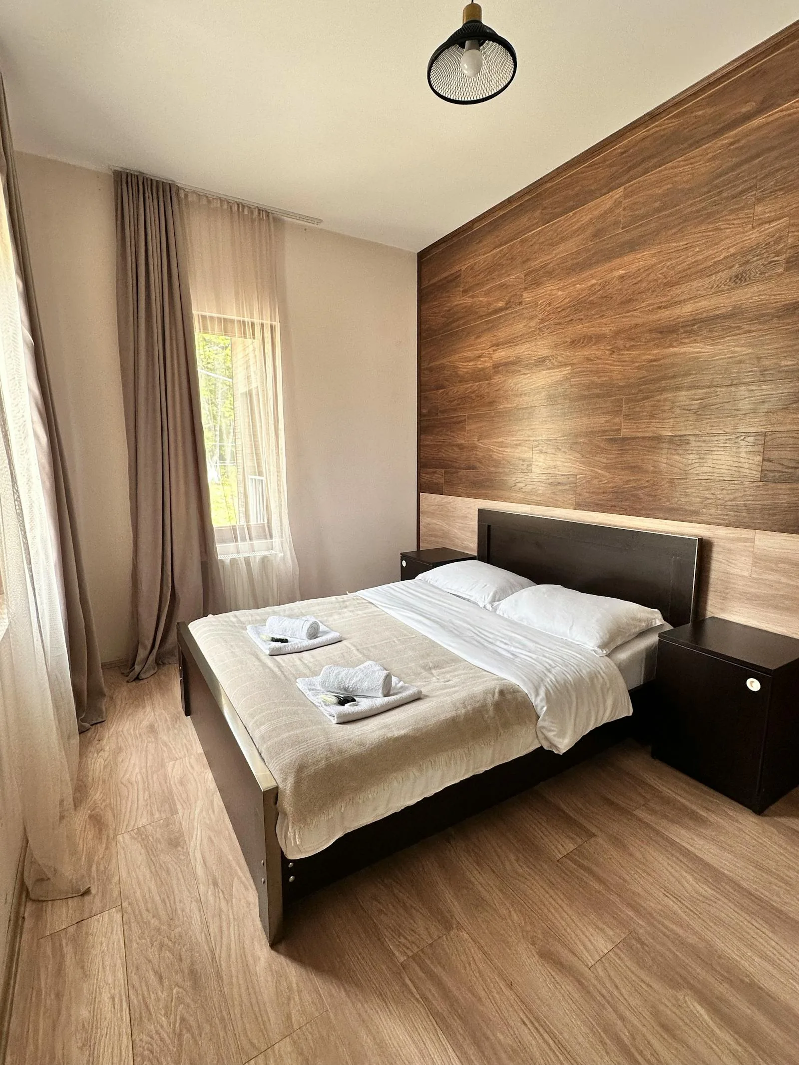 Simple bedroom with a bed on a solid wall, soft curtains, and open floor space