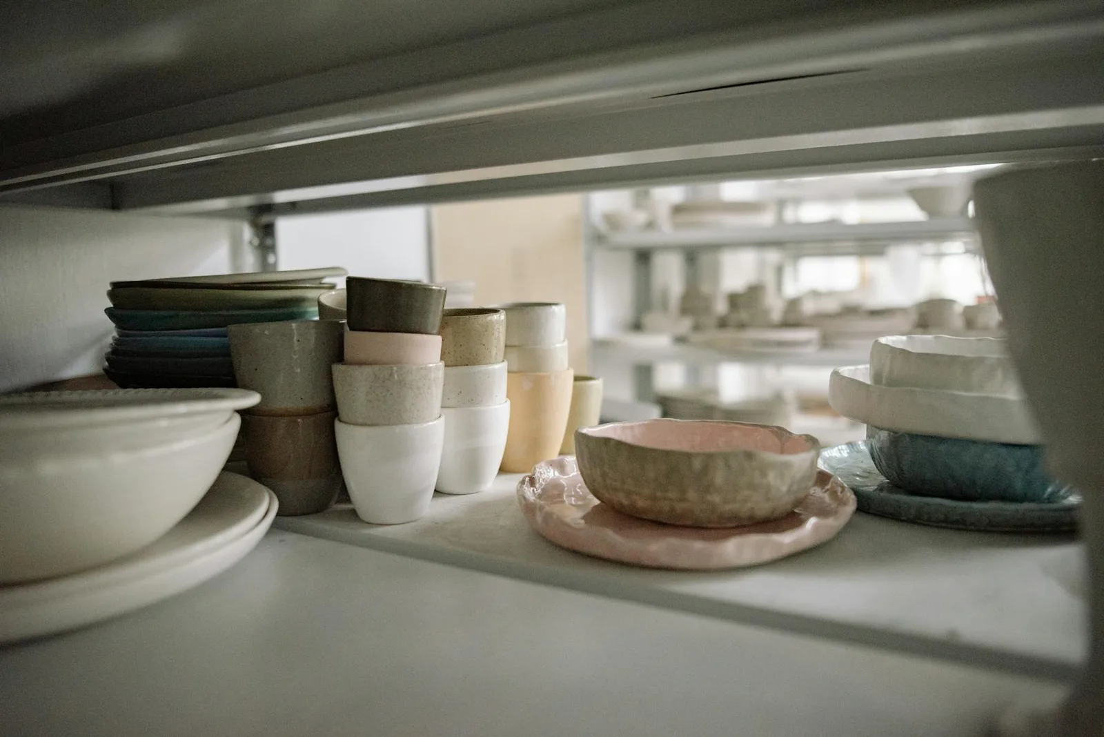 Stacked ceramic dishes and neutral pottery on a shelf