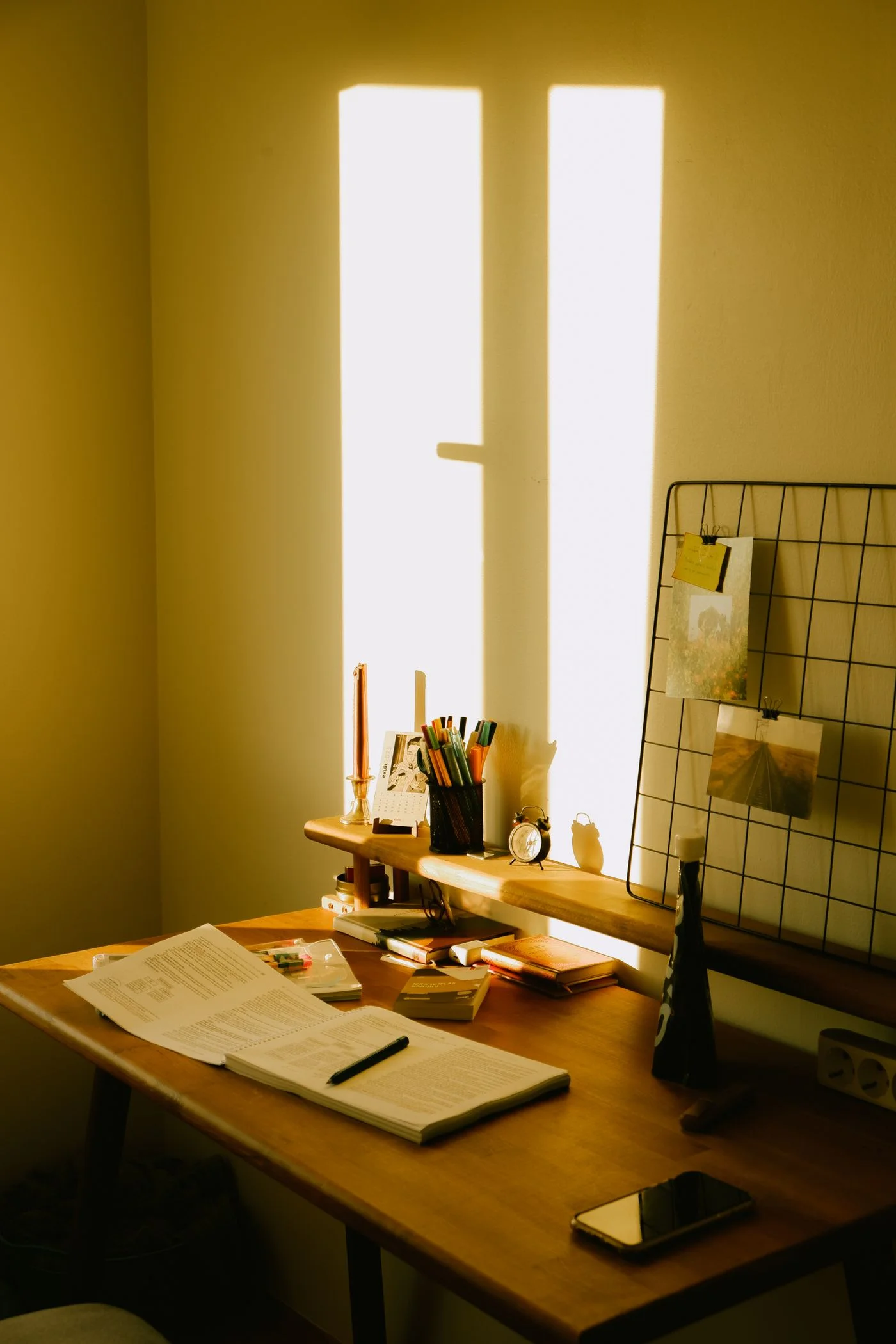 Direct sunlight falling across a home study desk, open books and stationery, with a bright window-shaped patch on the wall