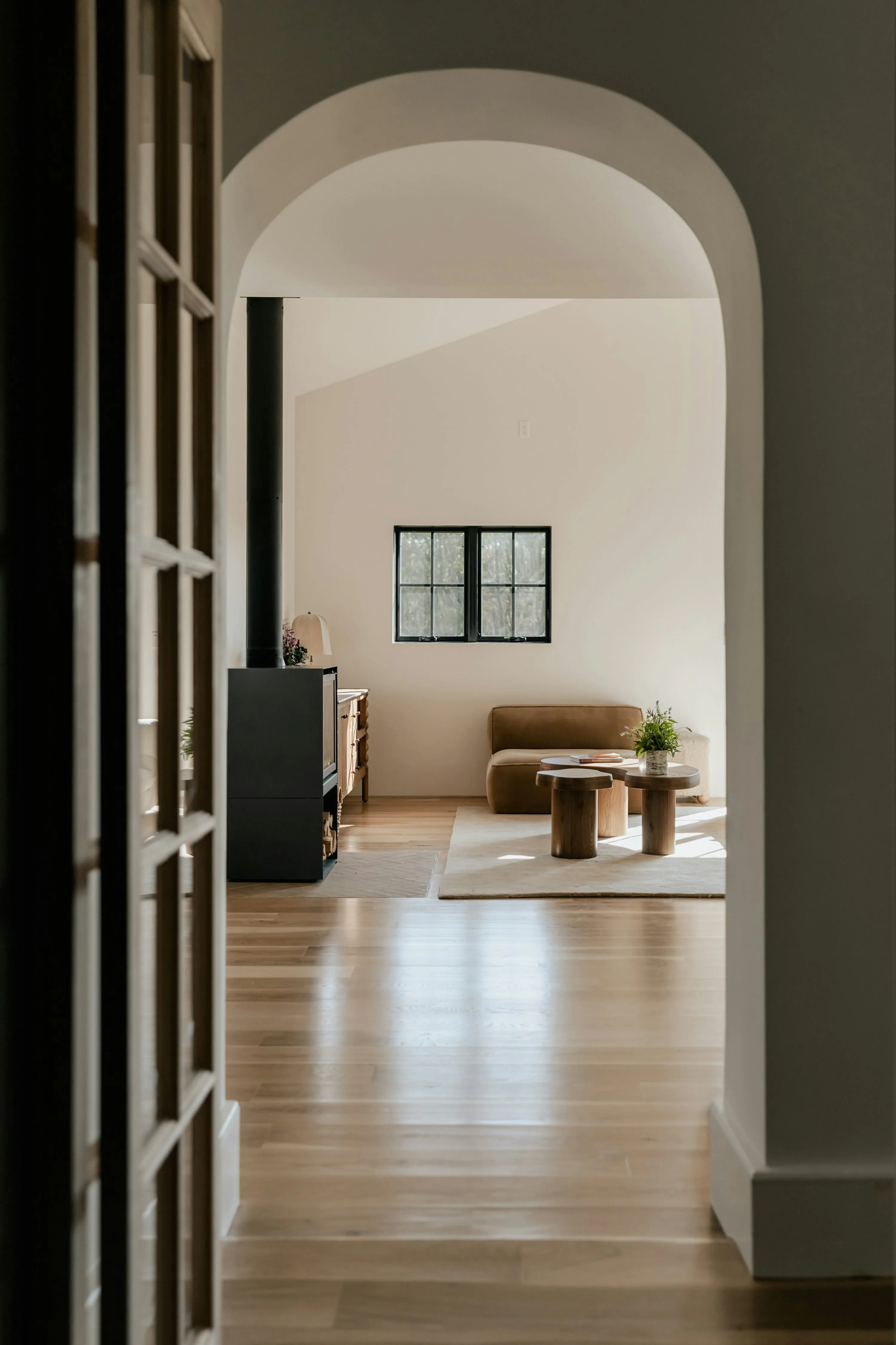 Arched threshold looking into a calm room with pale floors, a bench, and small tables