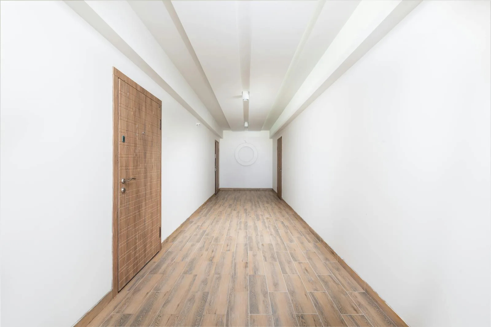 Long bright hallway with wood-look flooring, simple doors, and an open uncluttered walking route