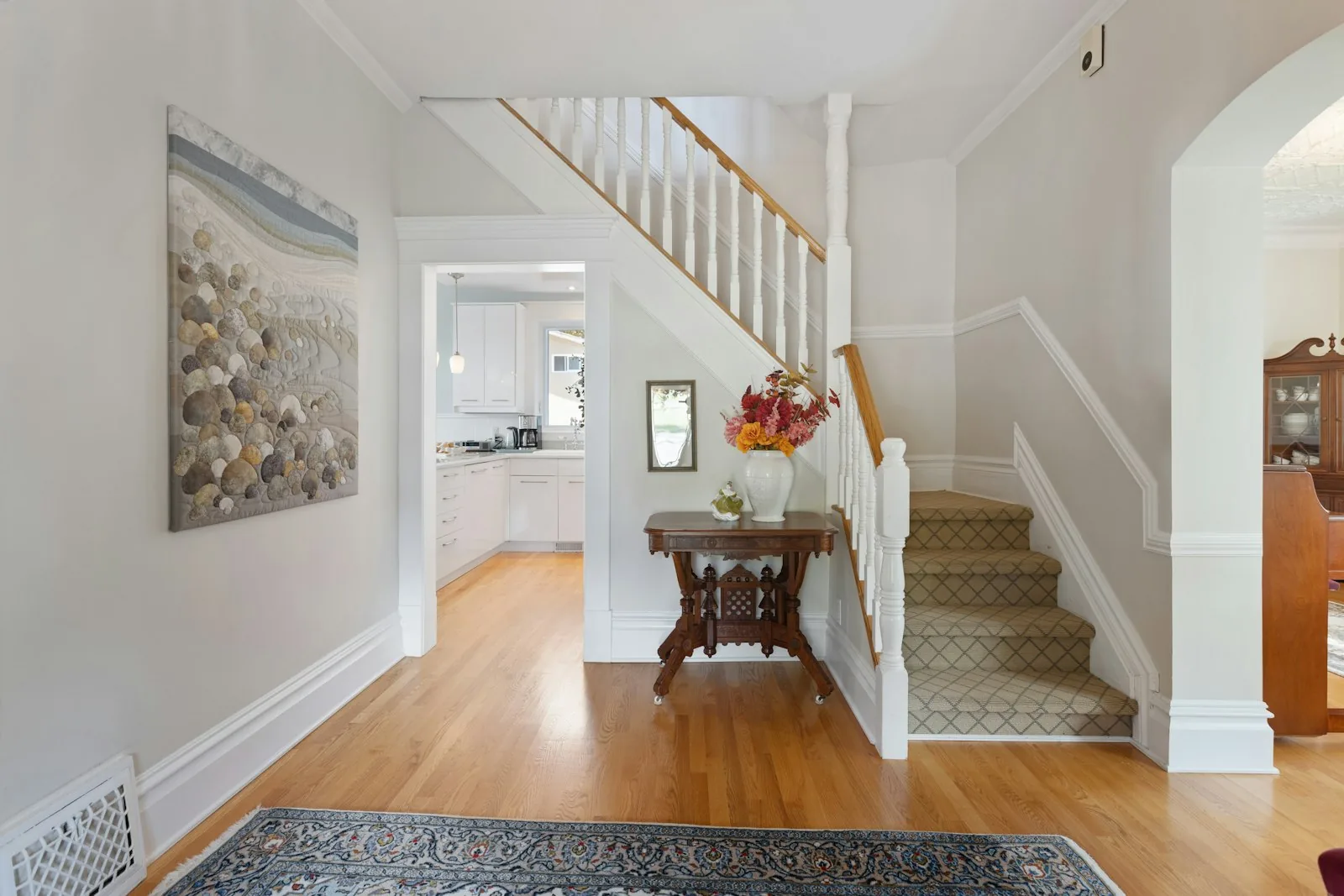 Traditional entry hall with staircase, rug, and a small wood console table with flowers