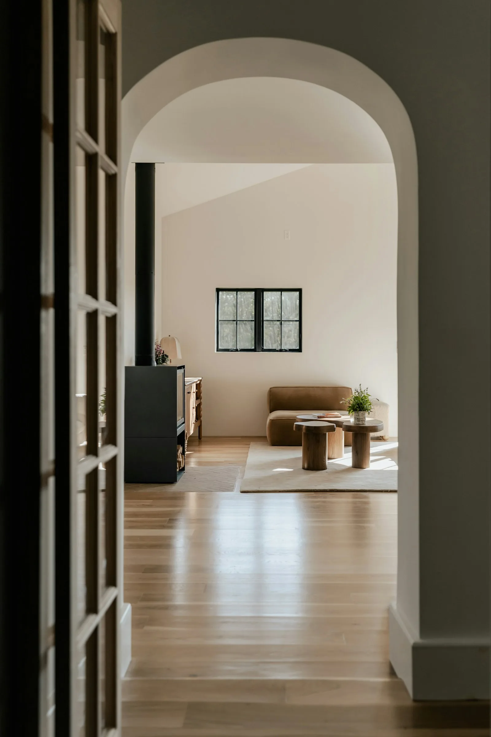 Arched interior threshold opening into a calm living area with wood floors and simple seating