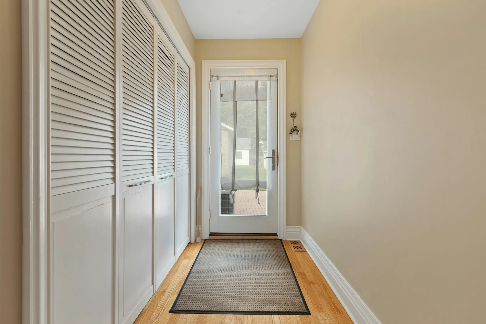 Narrow entry hall with closed closet doors, a runner rug, and a glass door at the end