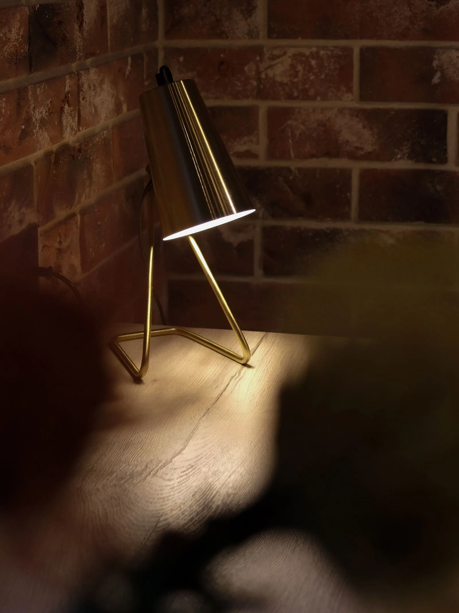 Small brass lamp directing a pool of light onto a wooden surface beside a brick wall