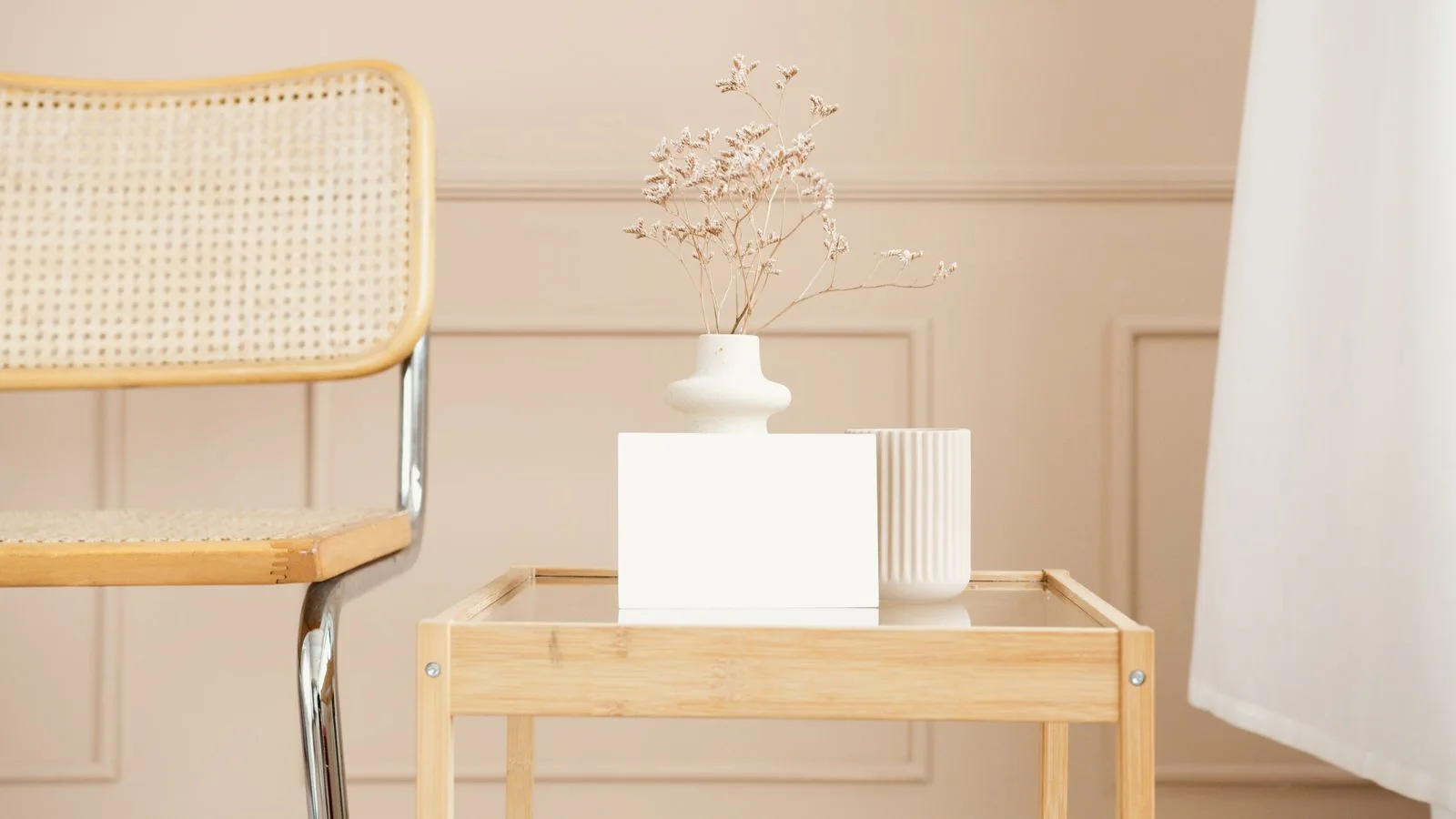 Cane-backed chair with metal legs beside a timber-and-glass table holding pale ceramic vessels