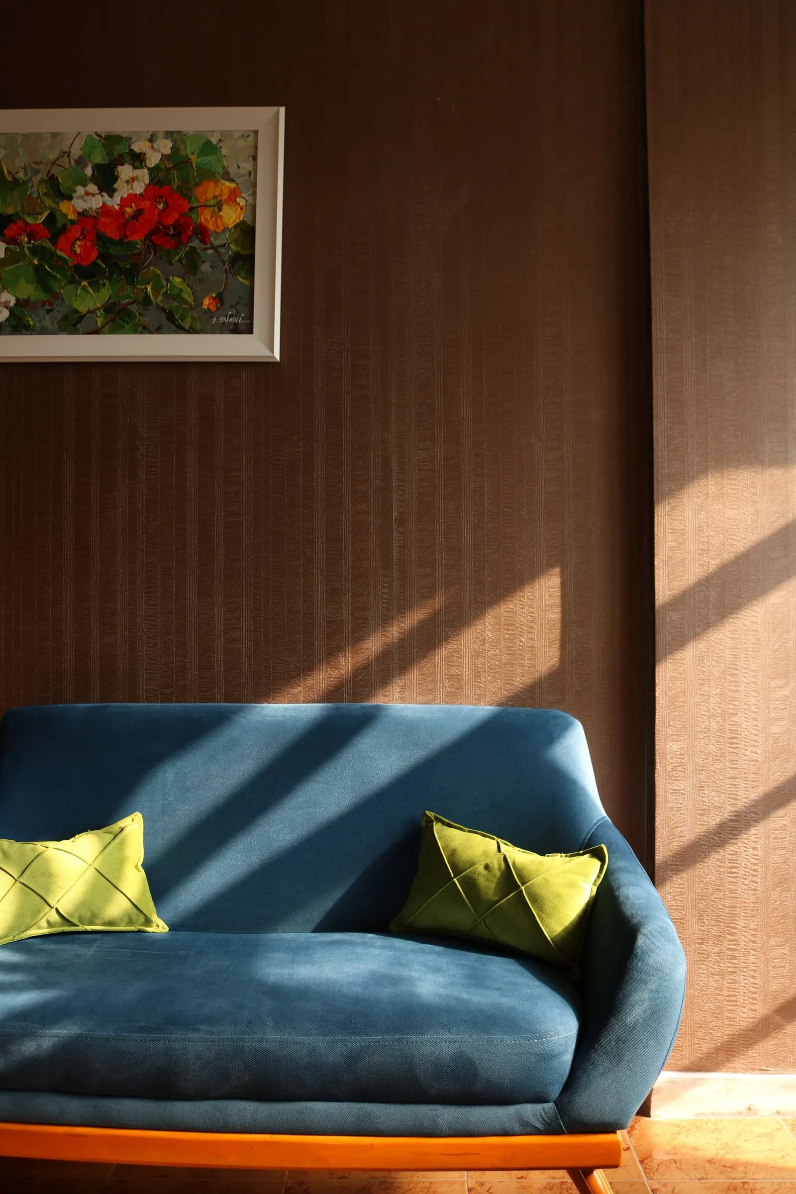 Blue sofa with yellow-green cushions against a timber-paneled wall in sunlight