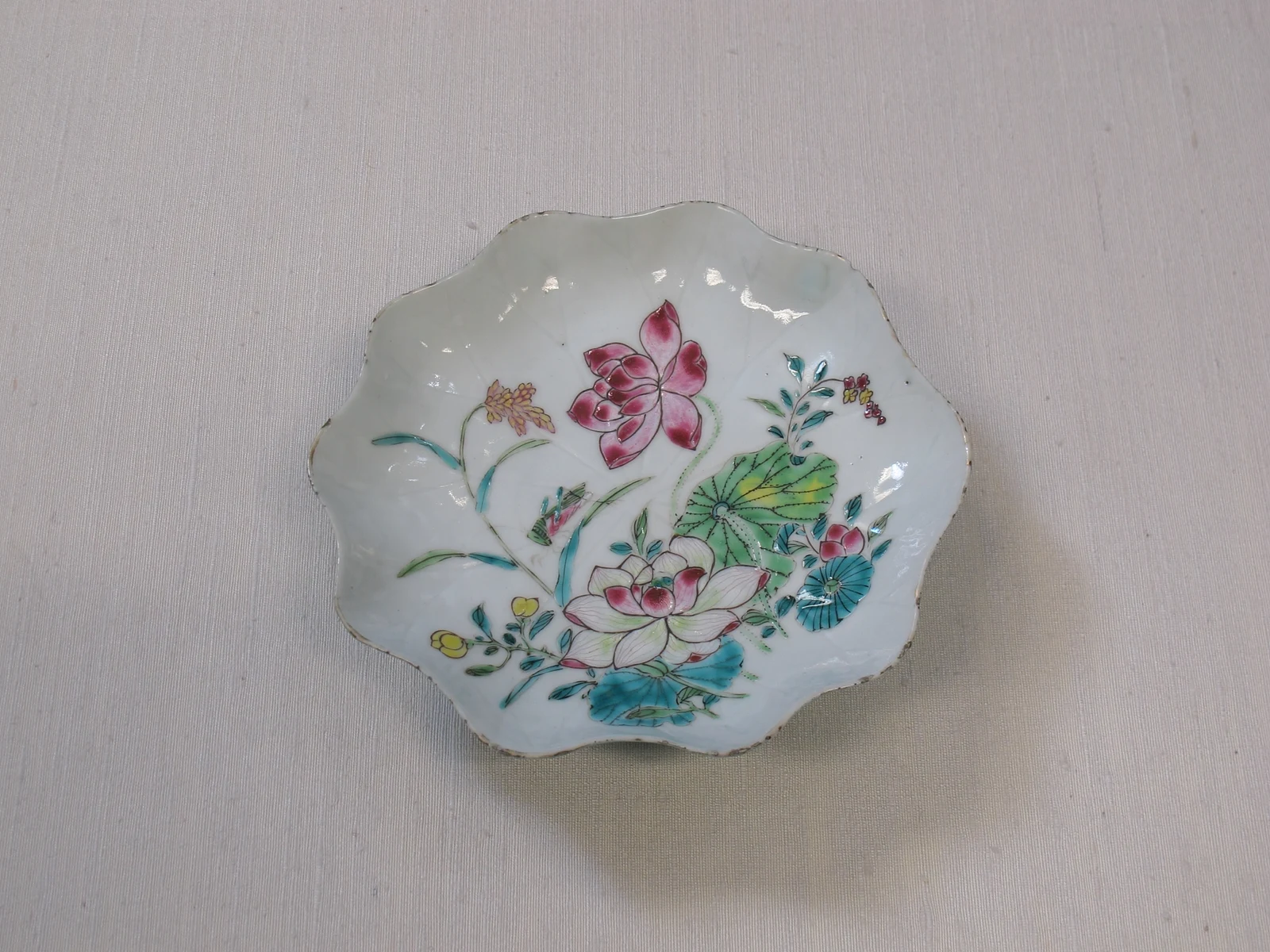 A scalloped Chinese porcelain dish painted with pink lotus flowers, rounded leaves and colorful foliage