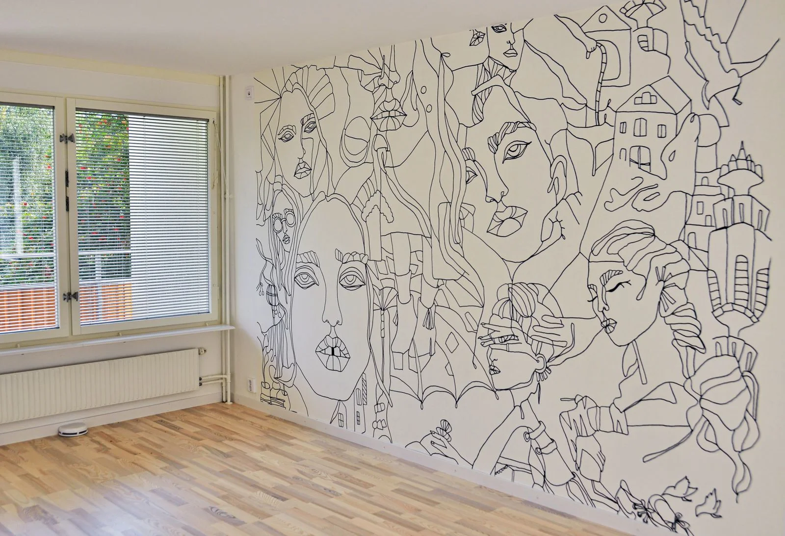 Wall-sized black line mural containing faces, hands, flowers and buildings in a sunlit room