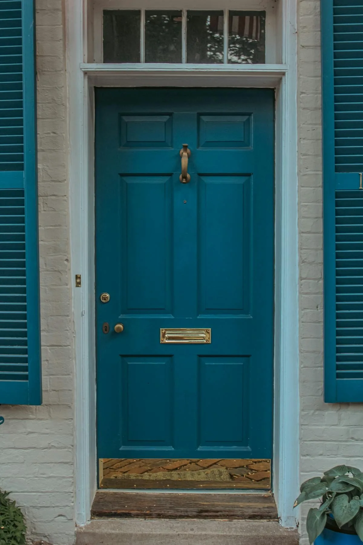 Muted blue front door with matching shutters on a light painted brick facade