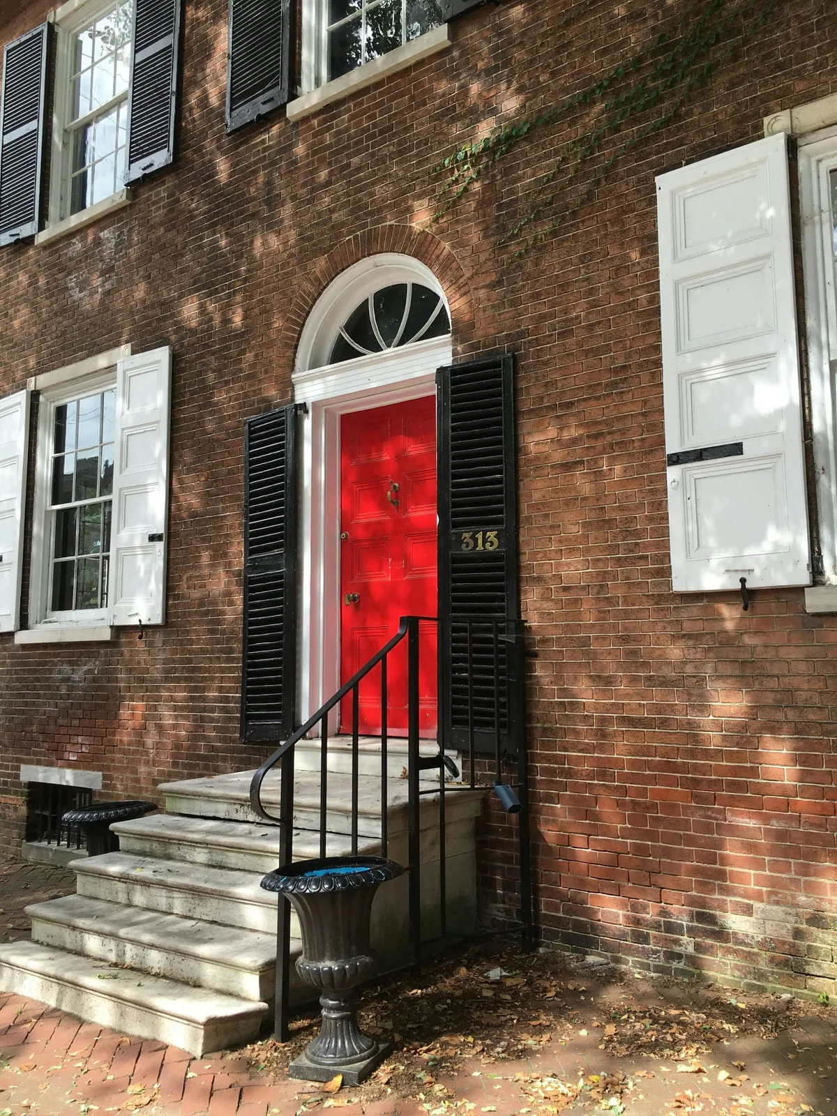 Red front door on a brick house with black shutters and stone entry steps