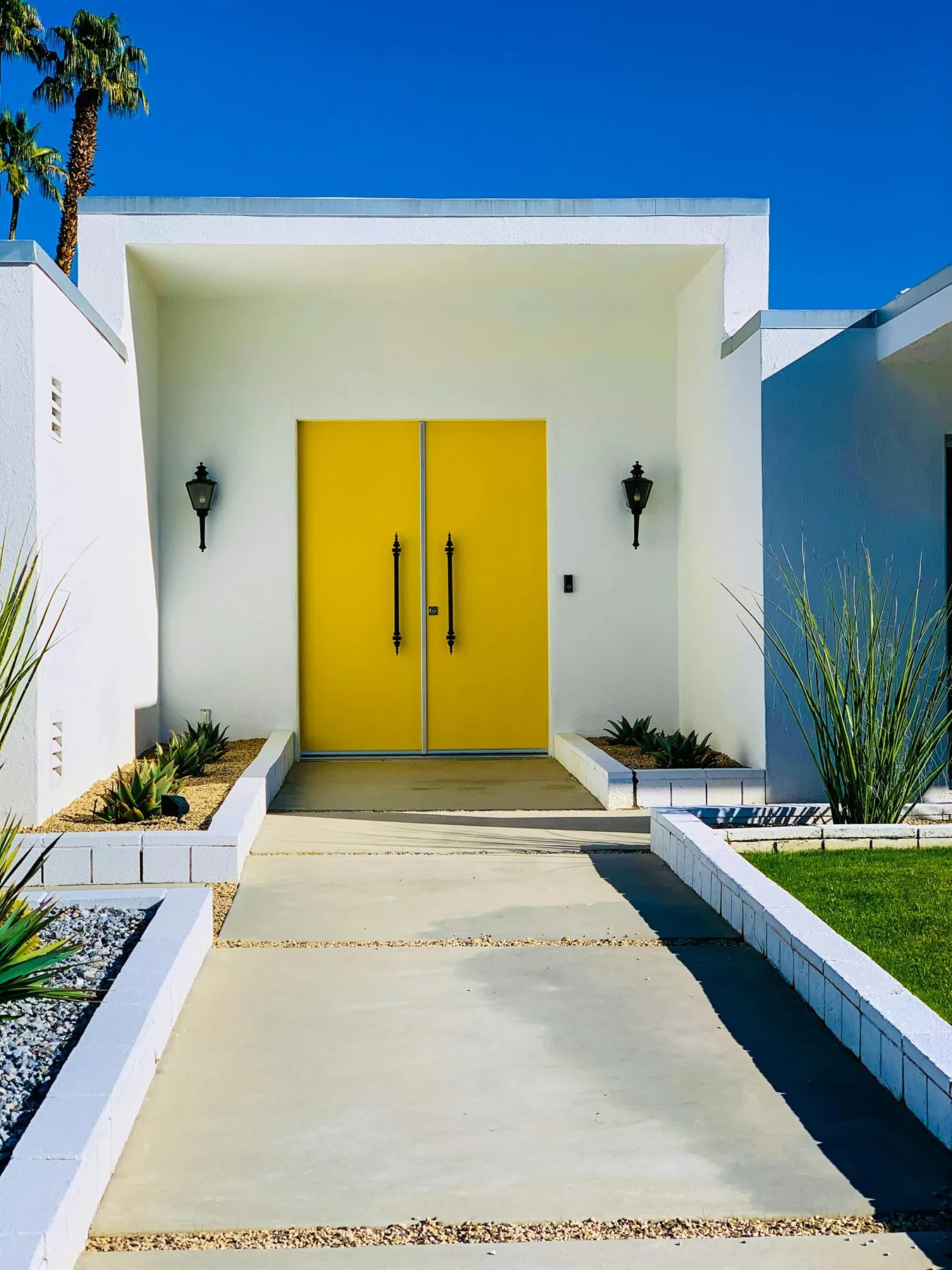 Modern white house with bold yellow front doors and a clear symmetrical walkway