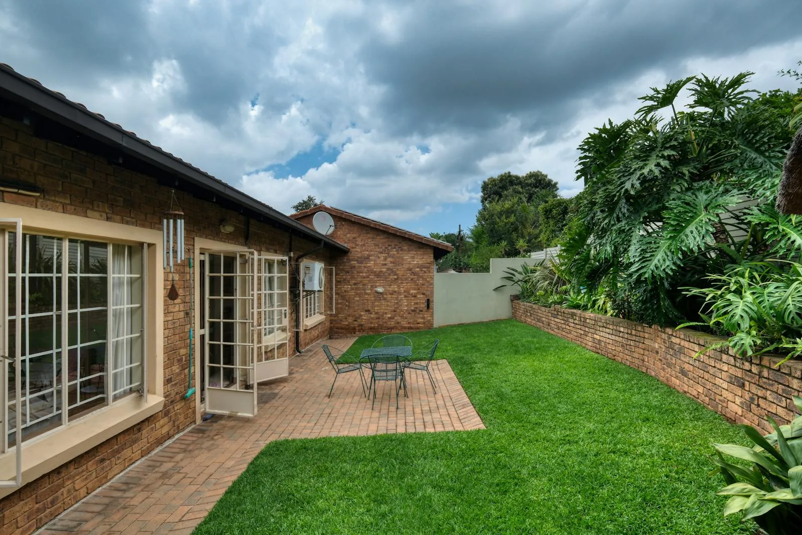 Patio and lawn with a simple outdoor table, chairs, and a planted boundary wall