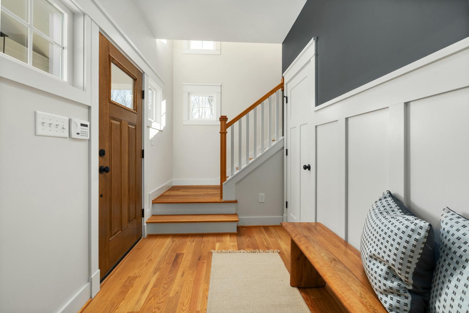 Bright entry hall with a wood front door, bench, rug, and strong natural light