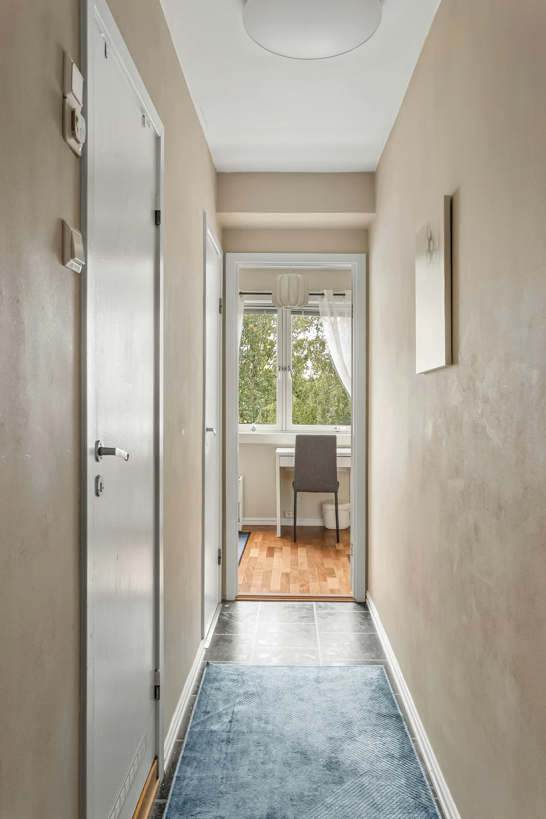 Narrow beige hallway with a blue runner, white doors along the left wall and a sunlit study beyond