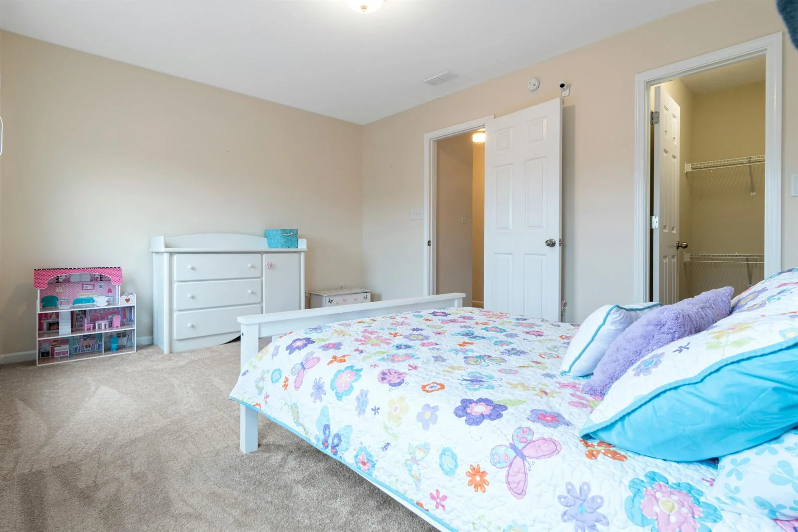 Kids bedroom with floral bedding, white furniture, and wide open carpeted floor