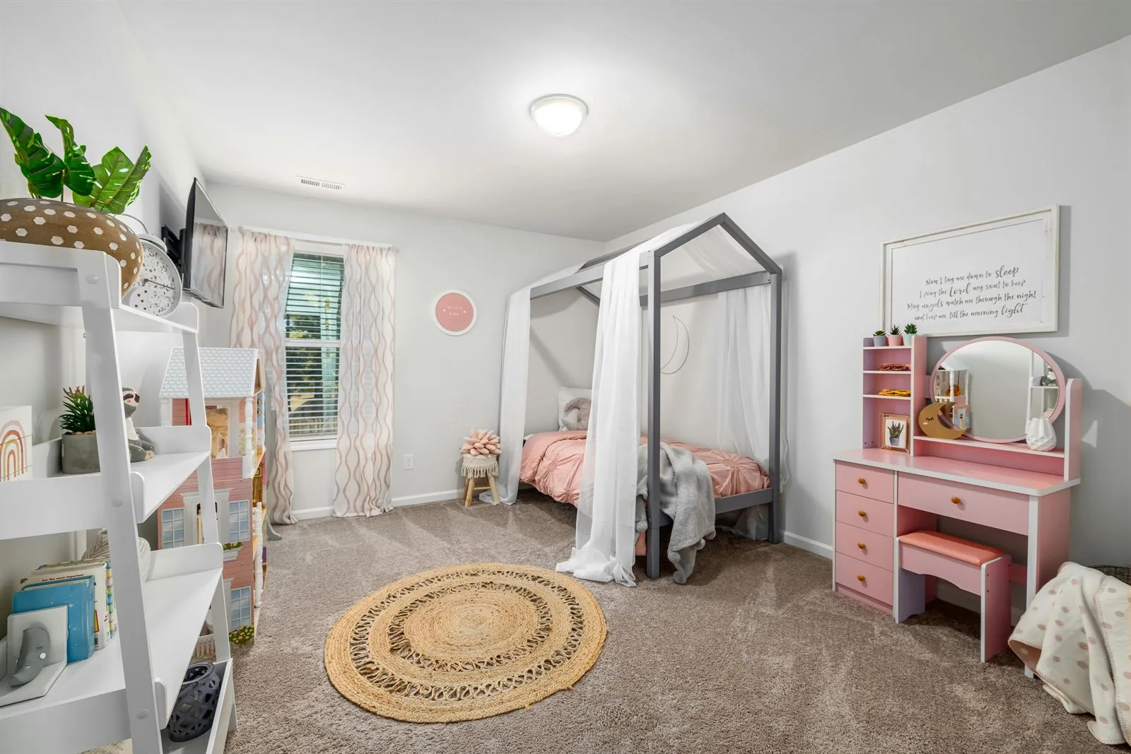 Kids room with canopy bed, pink desk vanity, open shelf, and a woven rug