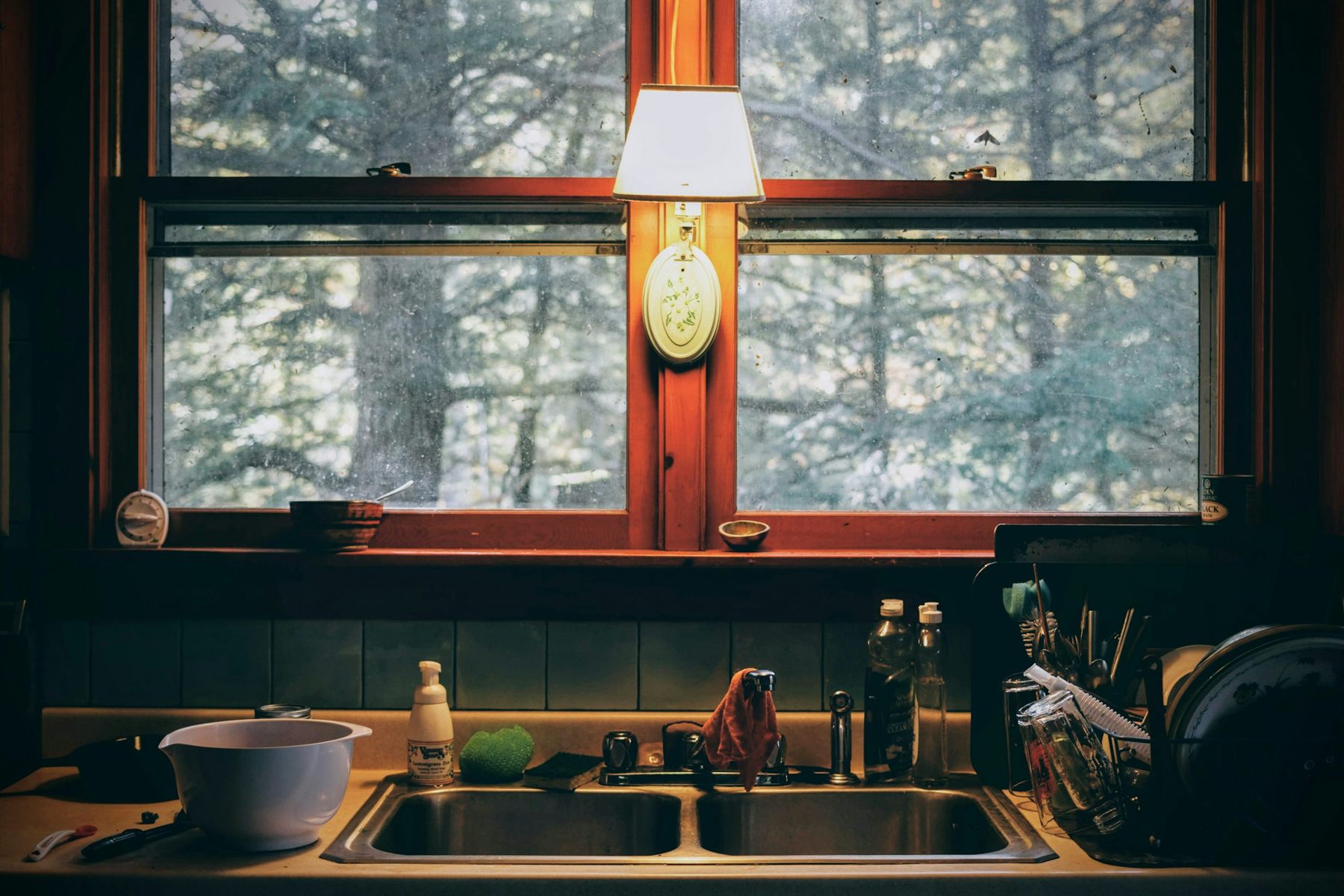 Kitchen sink beneath deep wood windows with darker tones and a moody evening feel