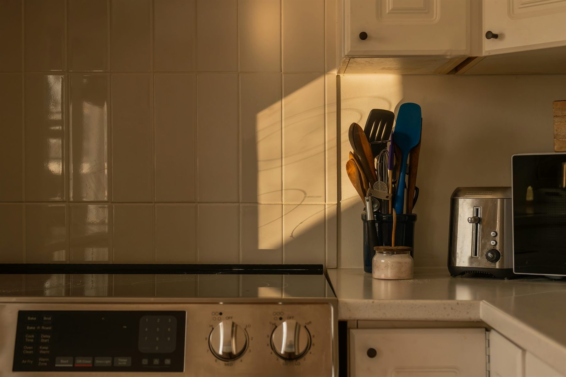 Kitchen counter at golden hour with cream tile, toaster, and utensils in soft warm light
