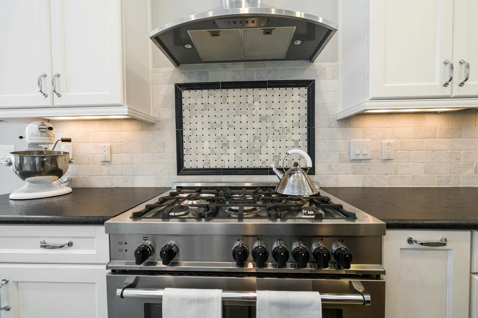 Kitchen stove with clear counters, clean burners, white cabinets, and task lighting