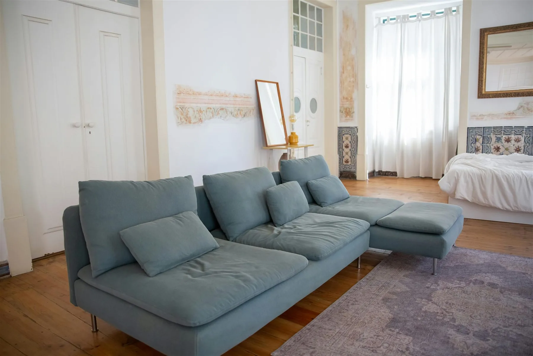 Living room with a dusty blue-green sofa, pale rug, and warmer wood floor