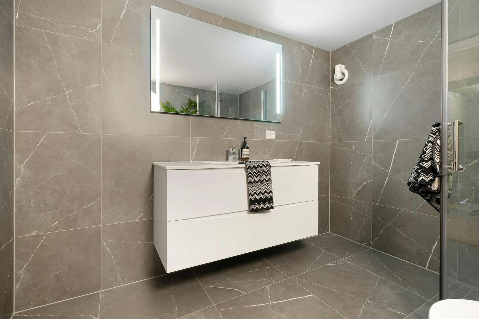 Glossy gray bathroom with cool tile, mirror, and white vanity