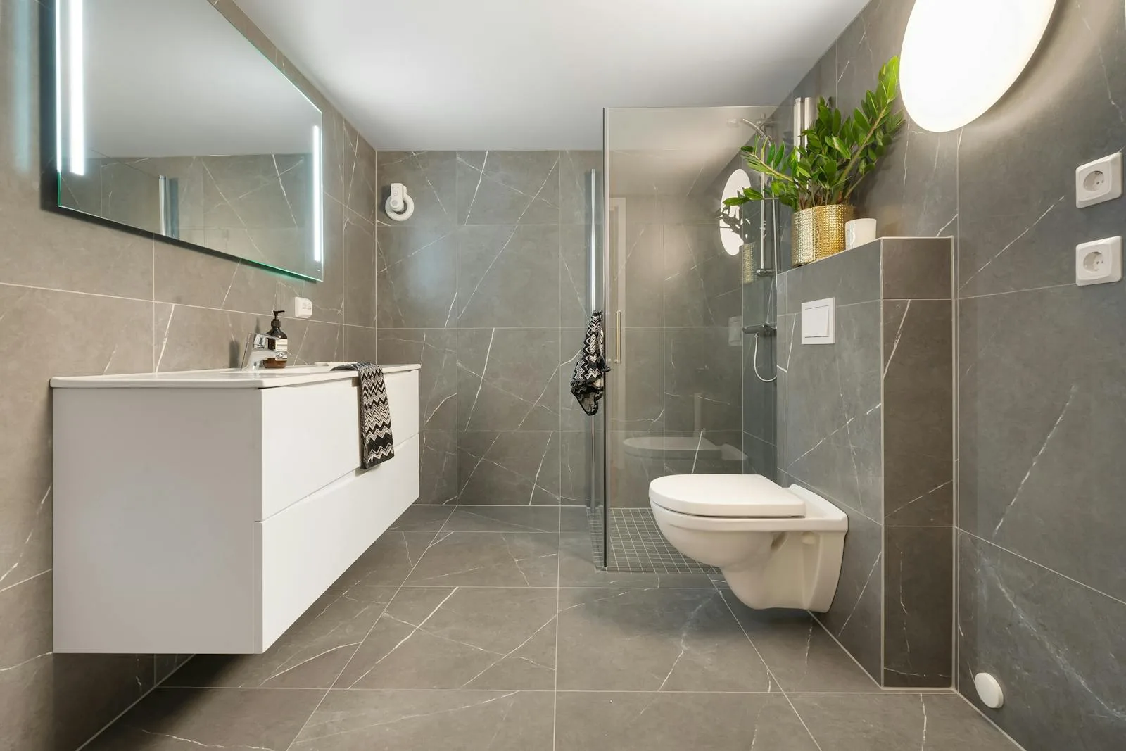 Gray tiled bathroom with white fixtures and a brass planter accent