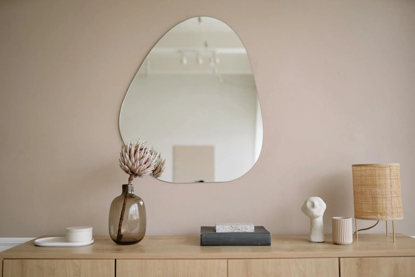 Softly styled cabinet with an irregular wall mirror, vase, and warm table lamp