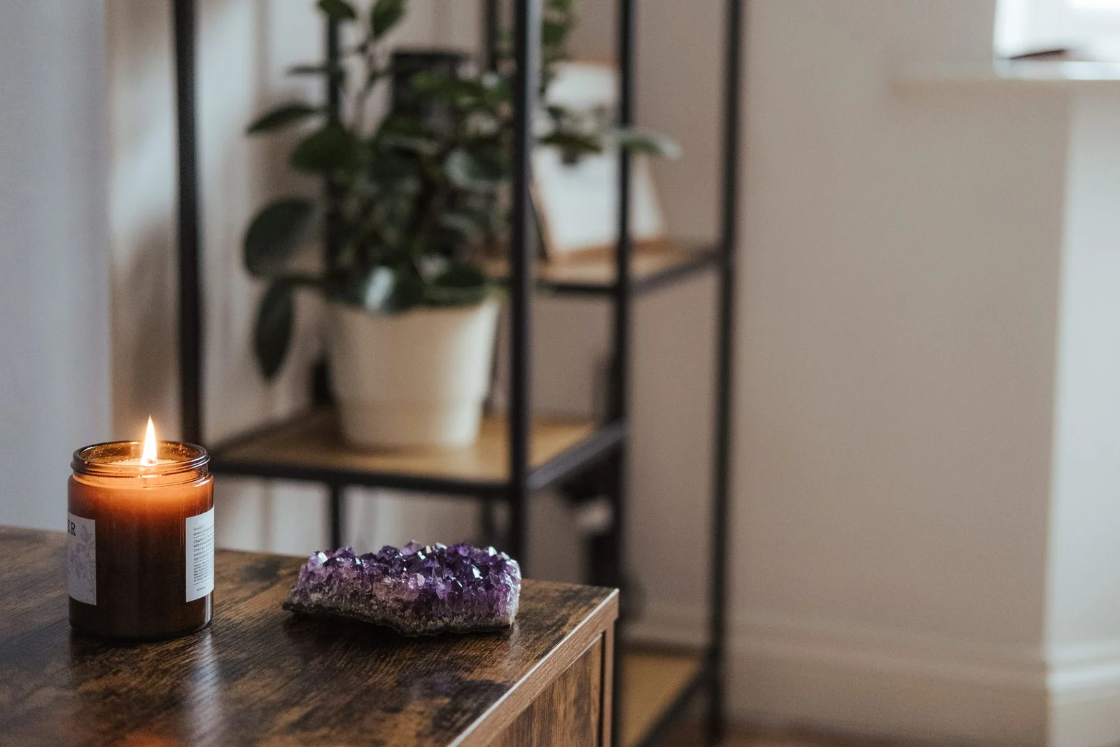 Small purple amethyst cluster on a timber cupboard beside a jar candle