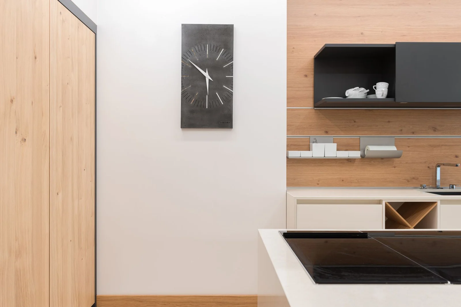 Rectangular dark wall clock beside timber kitchen cabinetry and a worktop