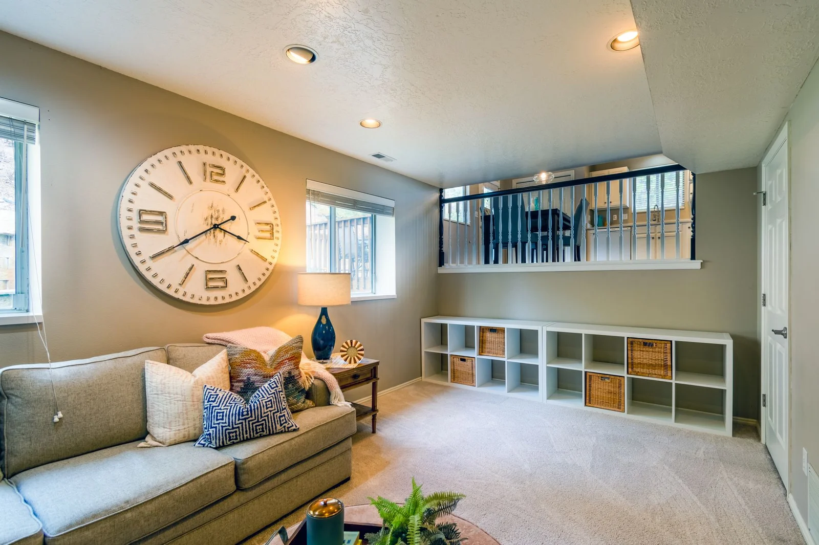 Oversized cream wall clock above a sofa between two living-room windows