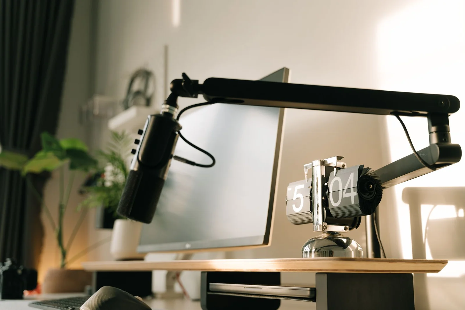 Flip clock beside a monitor beneath a microphone arm on a timber desk