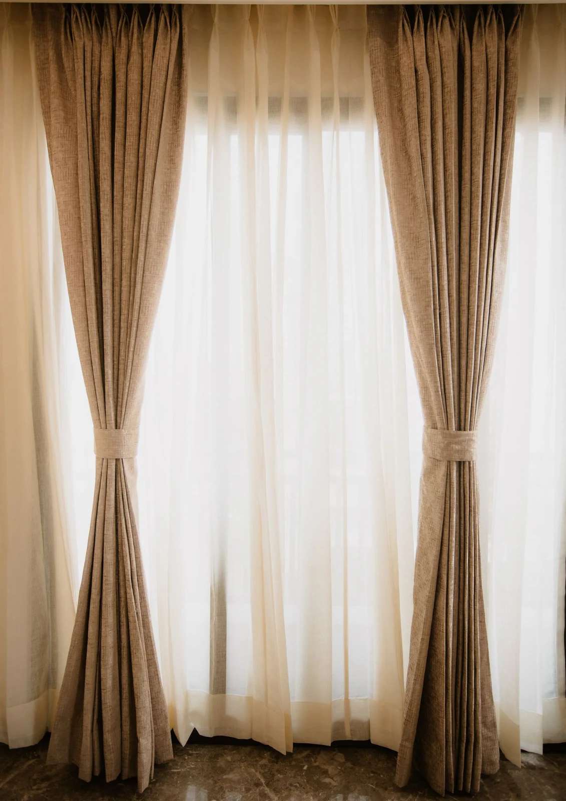 Beige curtain panels gathered beside a white sheer layer