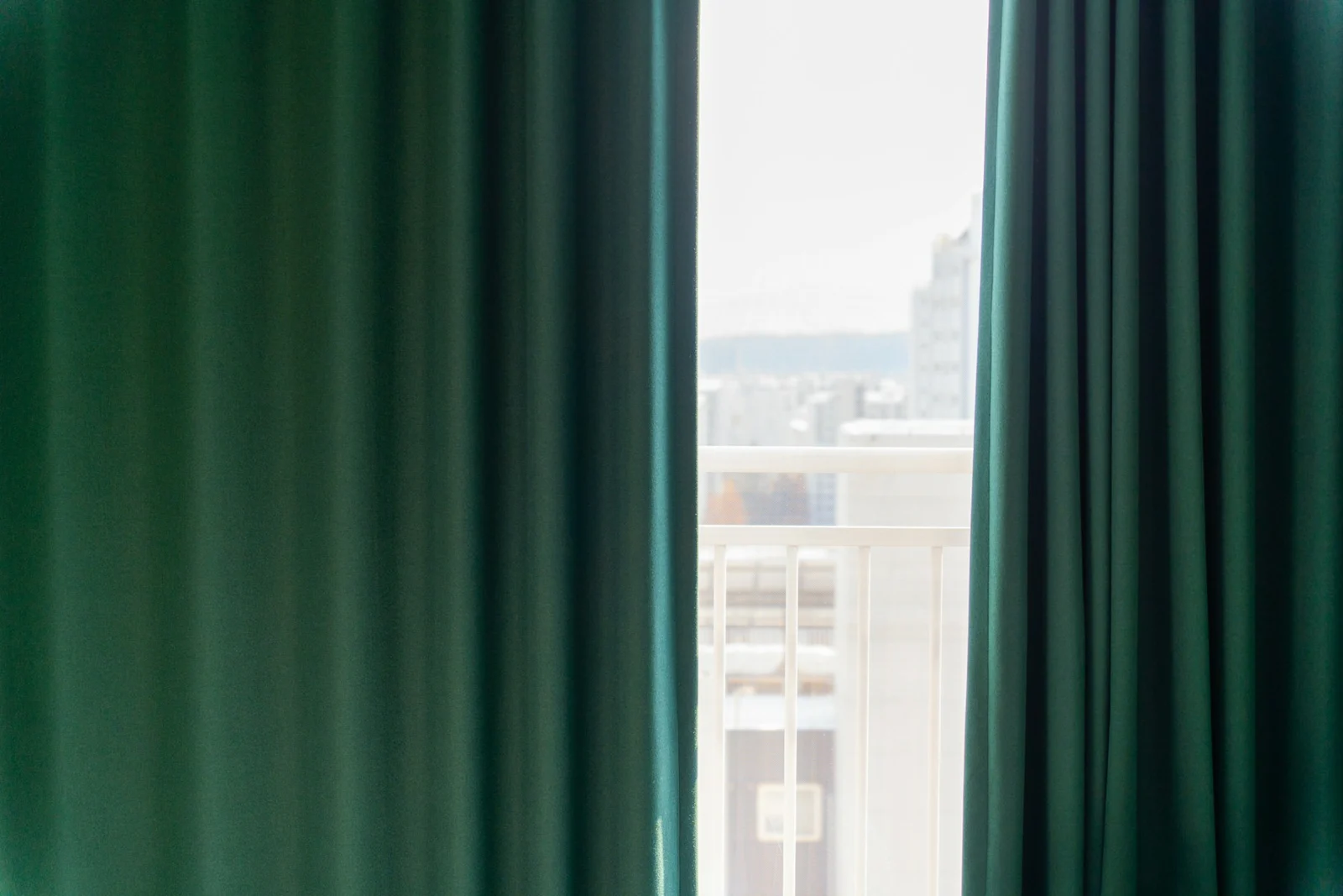 Close view of blue-green curtain panels beside a bright balcony window