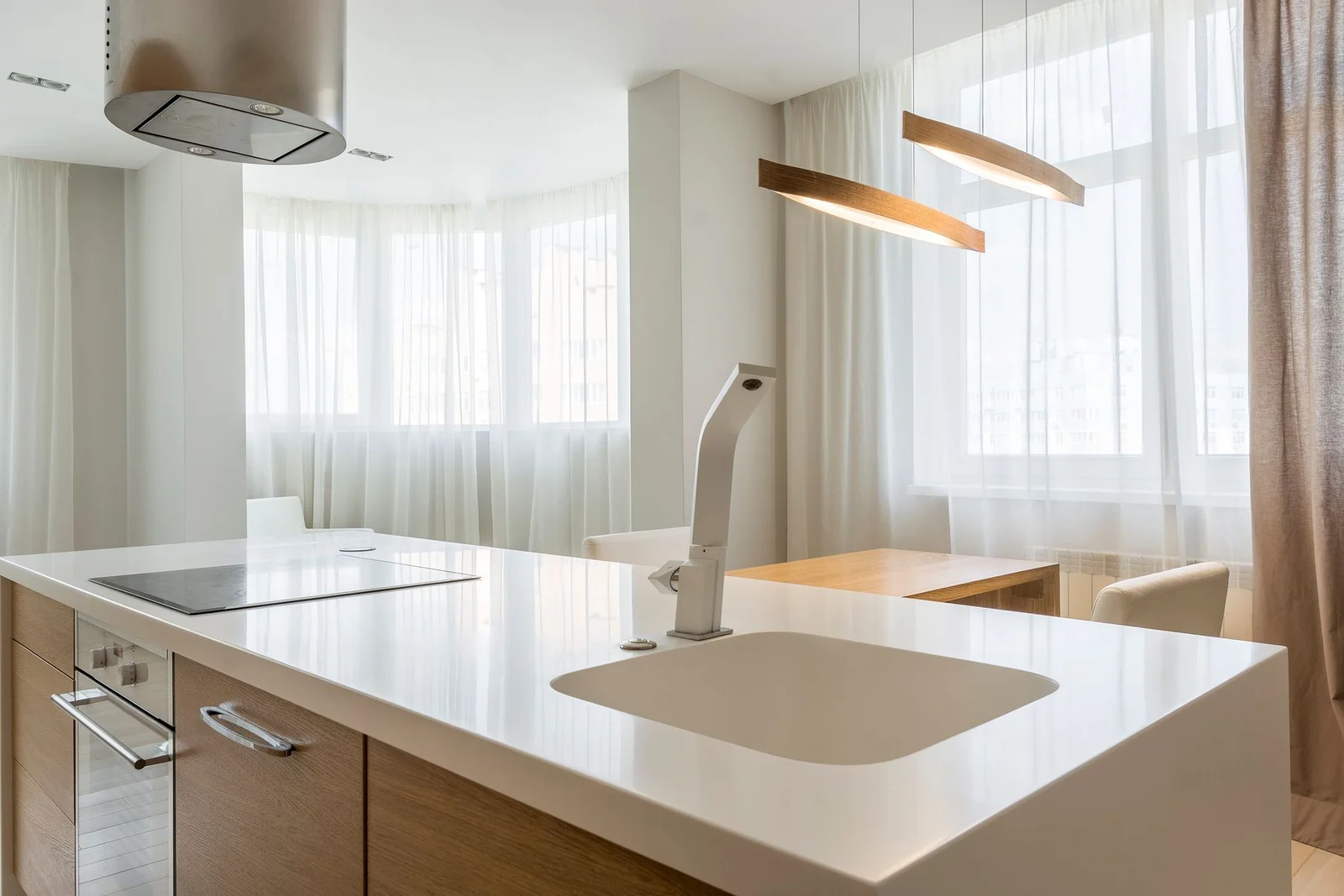 Sheer curtains at windows beyond a kitchen island and dining table